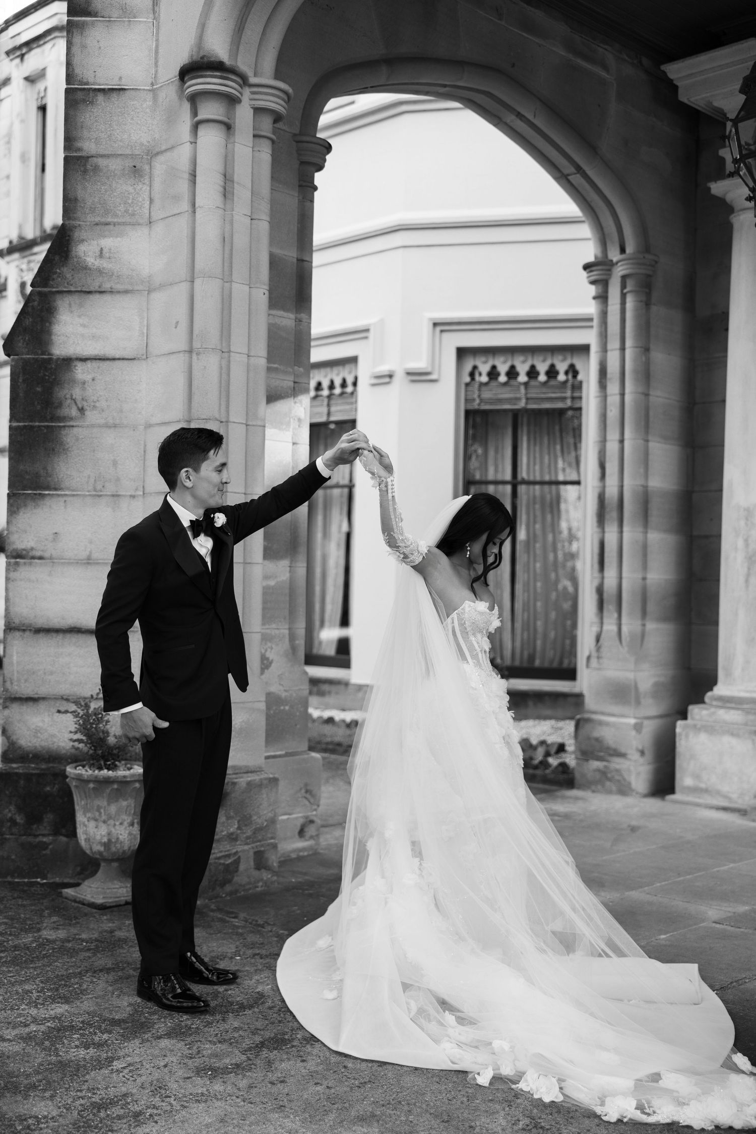 Groom twirls bride in flowing lace wedding gown under stone archway at historic castle wedding venue.