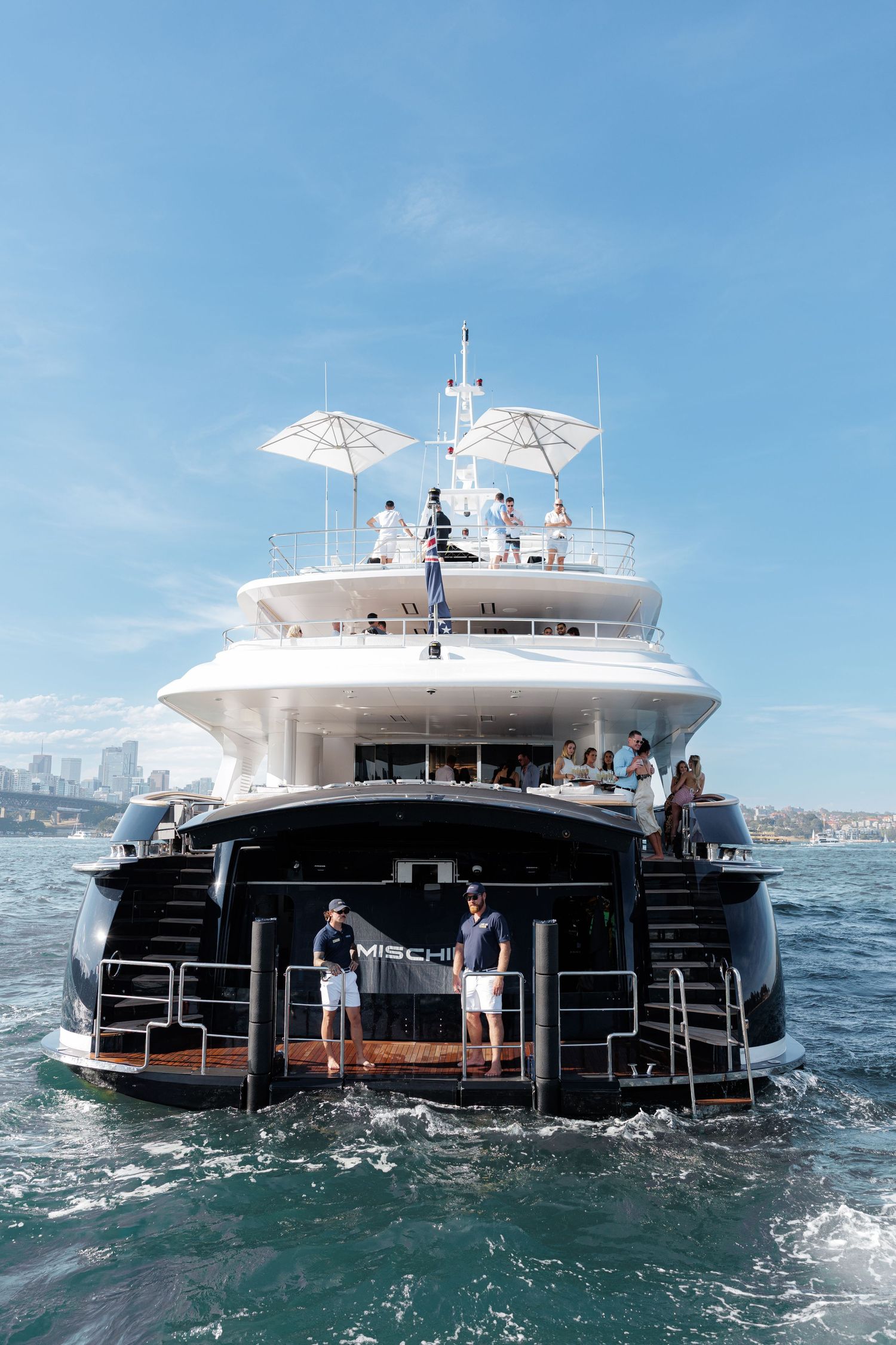 Luxury superyacht named Mischi cruises on blue waters with guests enjoying the upper deck on a sunny day.