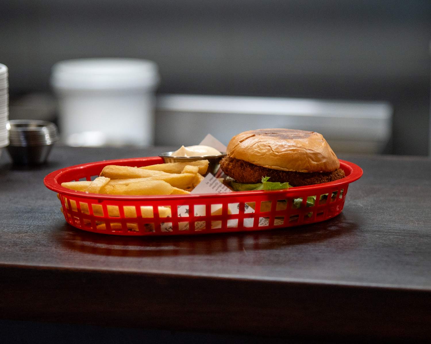 A classic burger with fries in a red plastic serving basket on a dark restaurant counter.