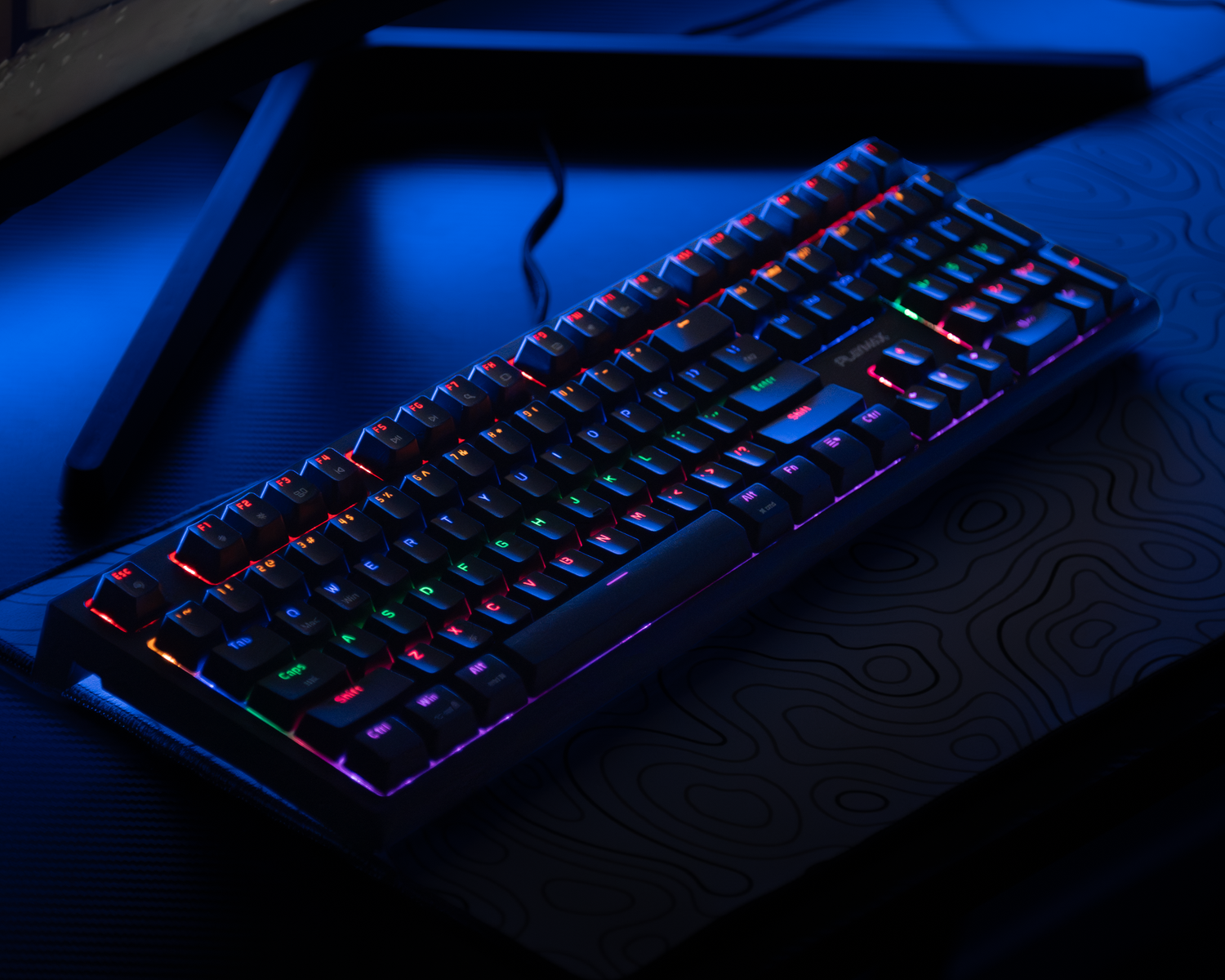 RGB mechanical gaming keyboard with multicolor backlighting on a dark desk in blue light.