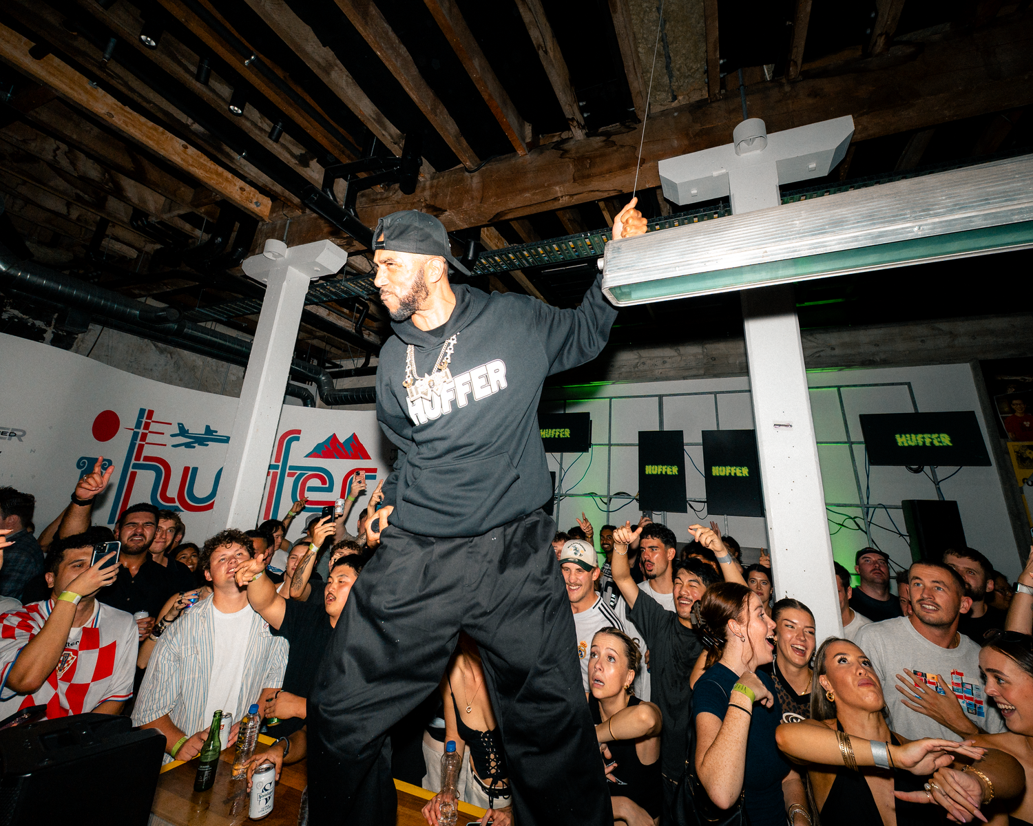Performer in black hoodie energizes crowd at lively indoor hip-hop concert event.