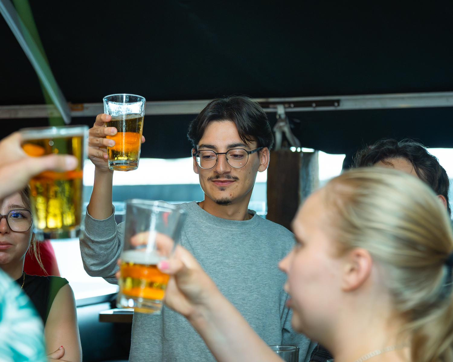 Group of friends raising glasses of beer in a cheerful toast at a bar.