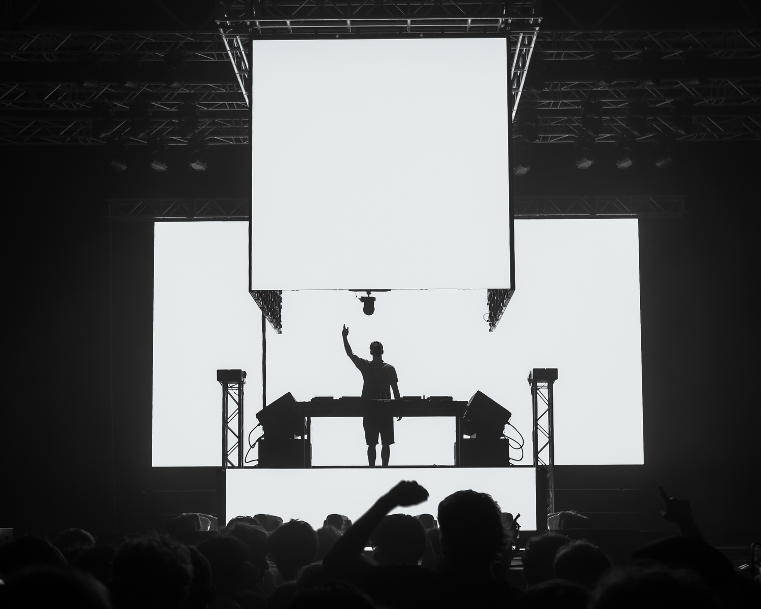 Black and white silhouette of a DJ on stage with a large screen backdrop at a live concert.