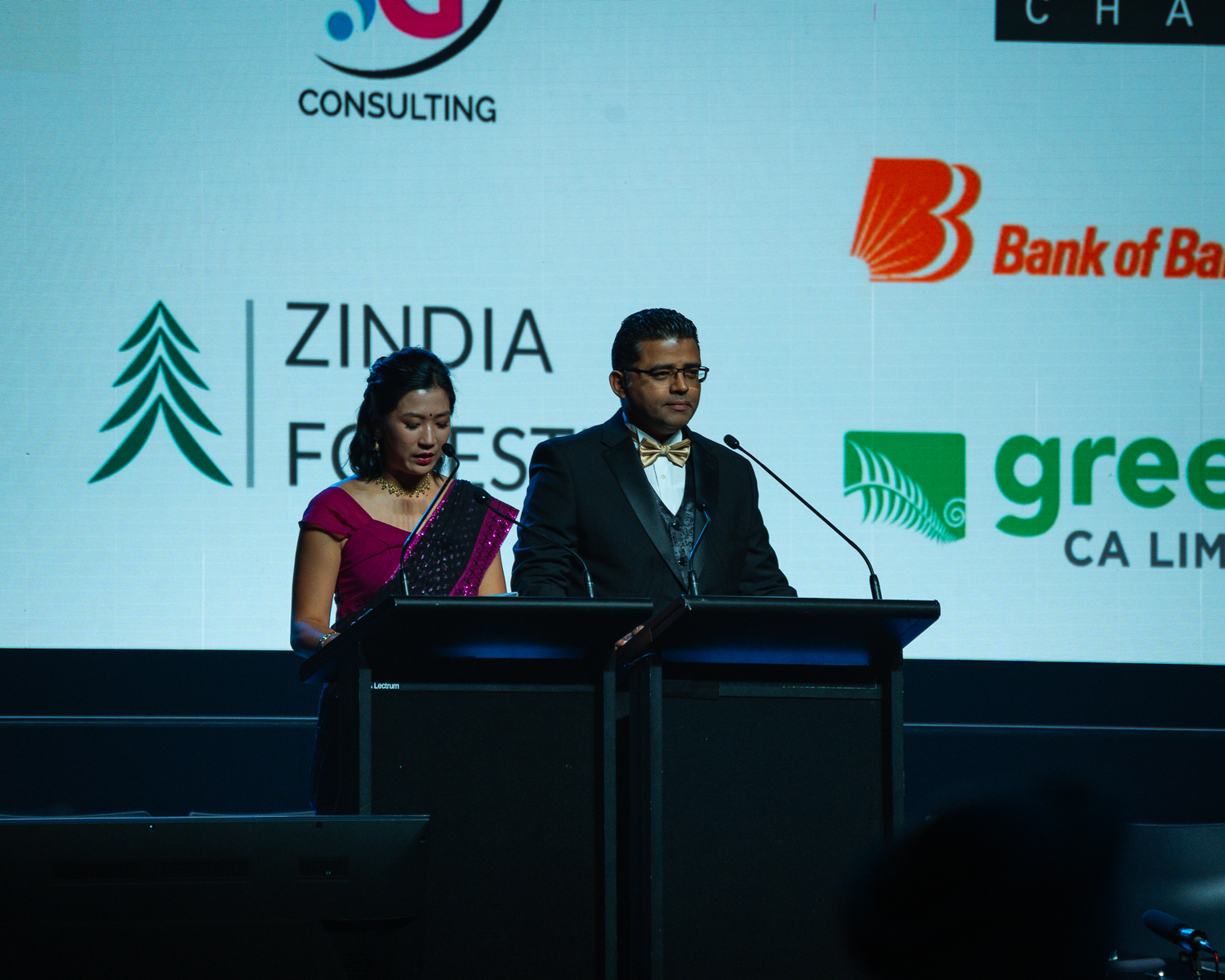 Two presenters speaking at a podium at the Zindia Forest event with sponsor logos displayed.
