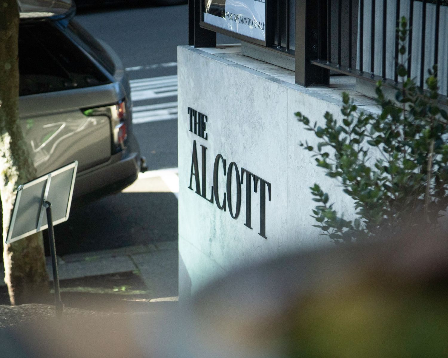 Exterior sign of The Alcott venue with a parked car visible in the background.