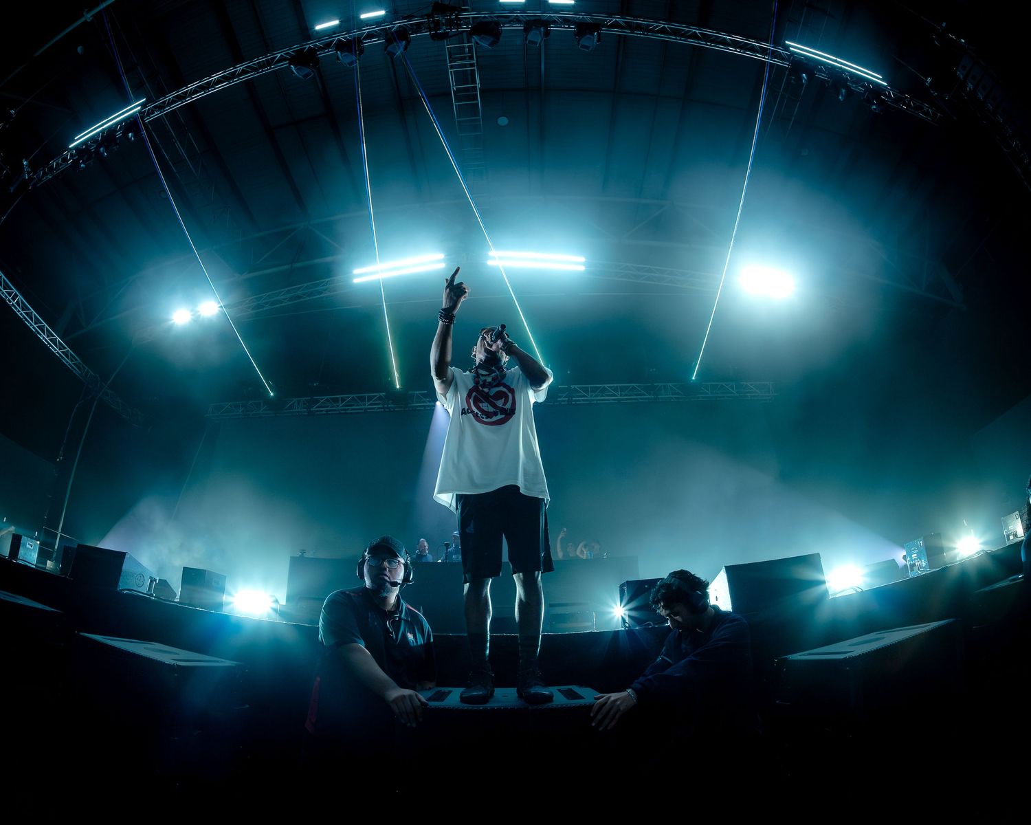 DJ performing on stage with dramatic teal lighting and fisheye lens at a live music event.