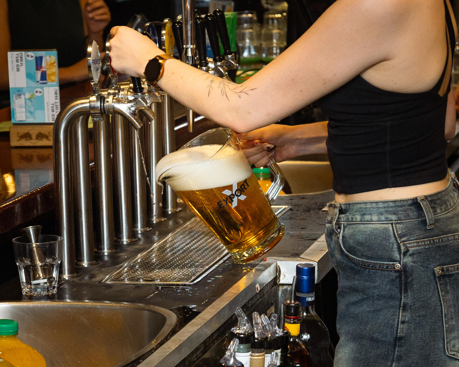 Bartender pouring a frothy draft beer at a busy bar counter.