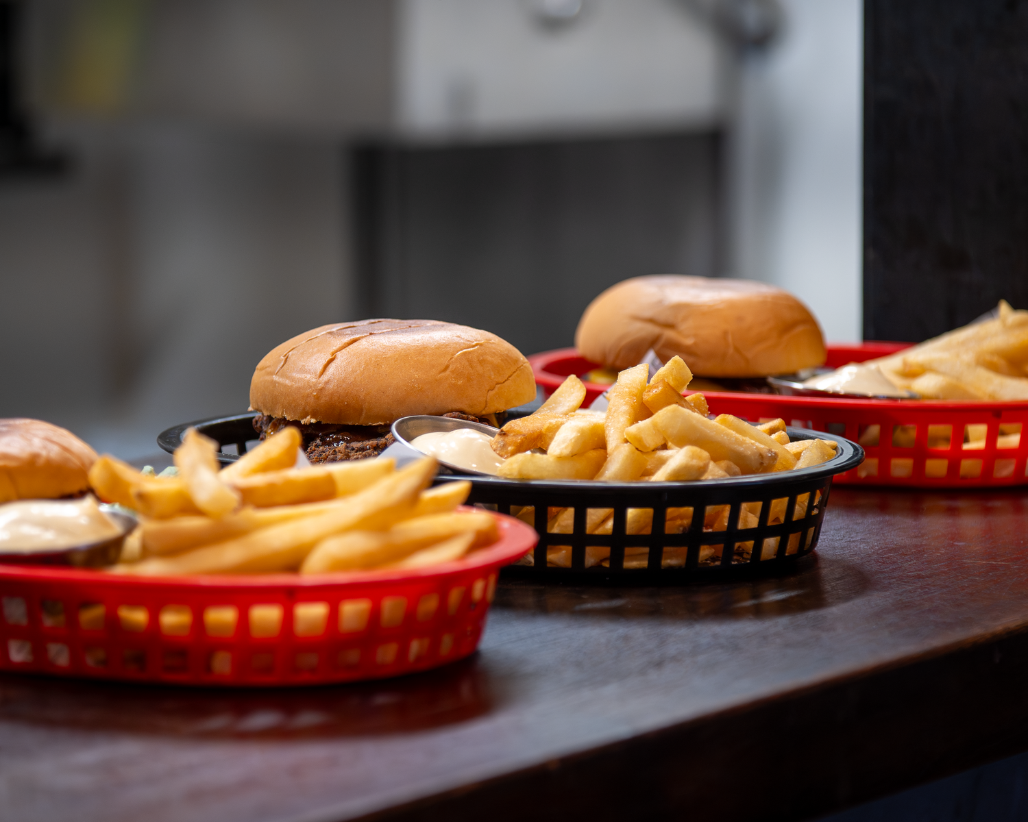 Multiple burgers and crispy fries served in red baskets lined up on a restaurant counter.