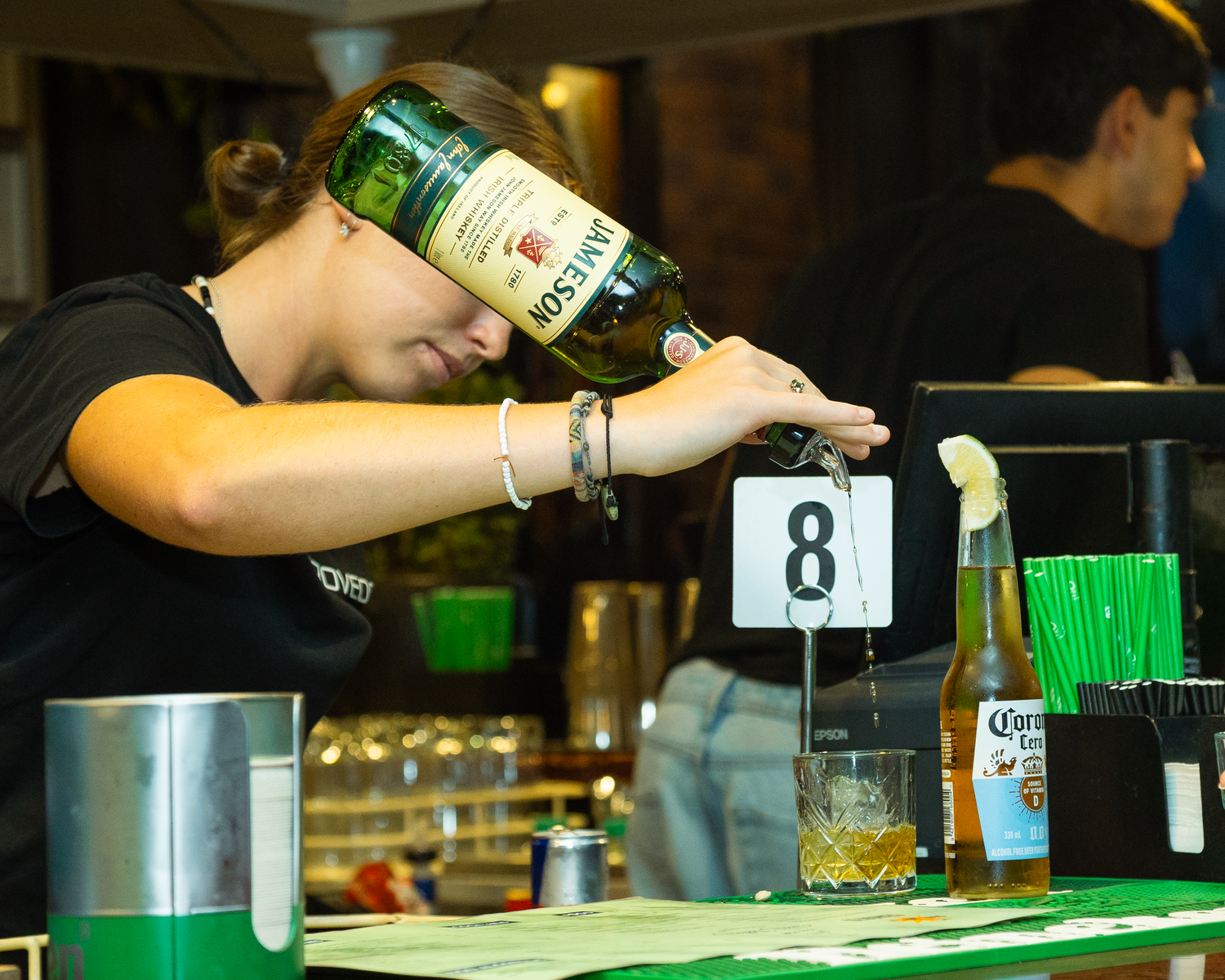 Bartender pouring Jameson whiskey into a glass at a numbered bar station.