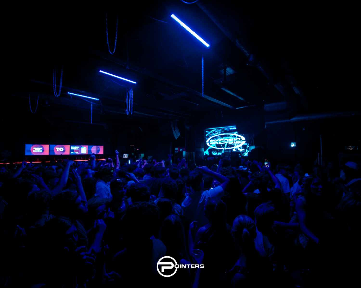 Packed nightclub crowd dancing under blue neon lights atInters club with glowing stage backdrop.