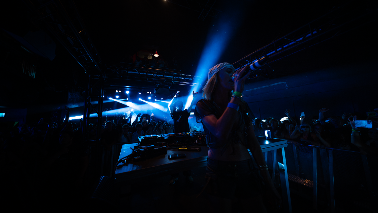 DJ performs under dramatic blue stage lights at a packed nightclub concert event.