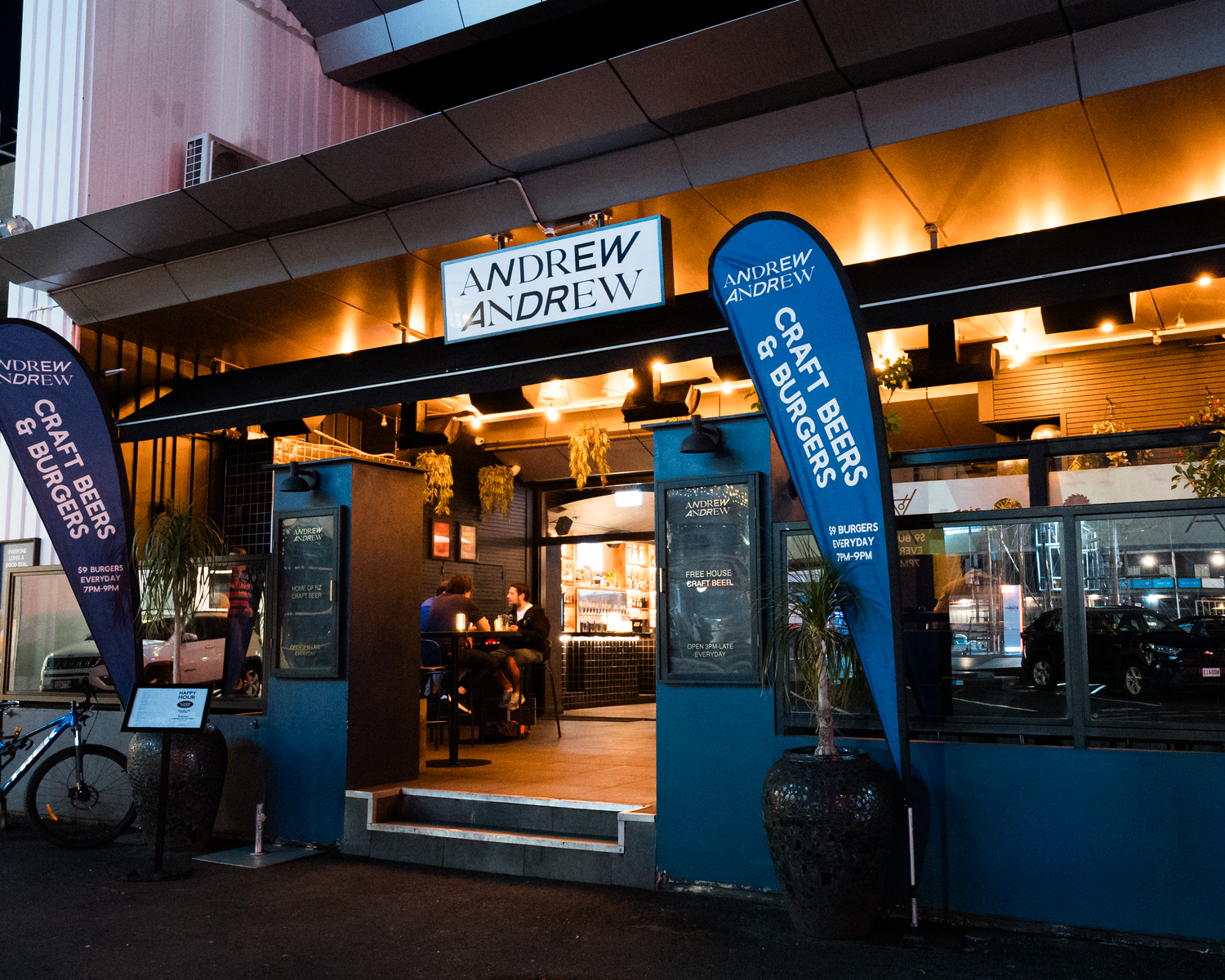 Andrew and Andrew restaurant exterior at night with blue signage and craft beer and burgers banners.