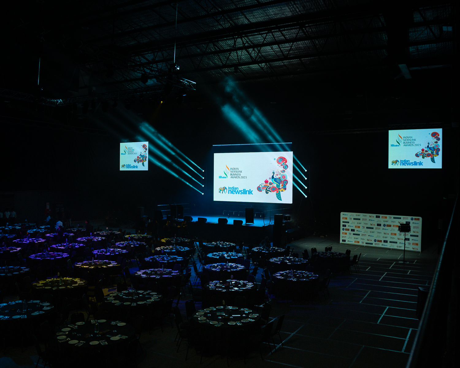 Large event venue with round tables, stage screens, and dramatic blue and purple lighting.
