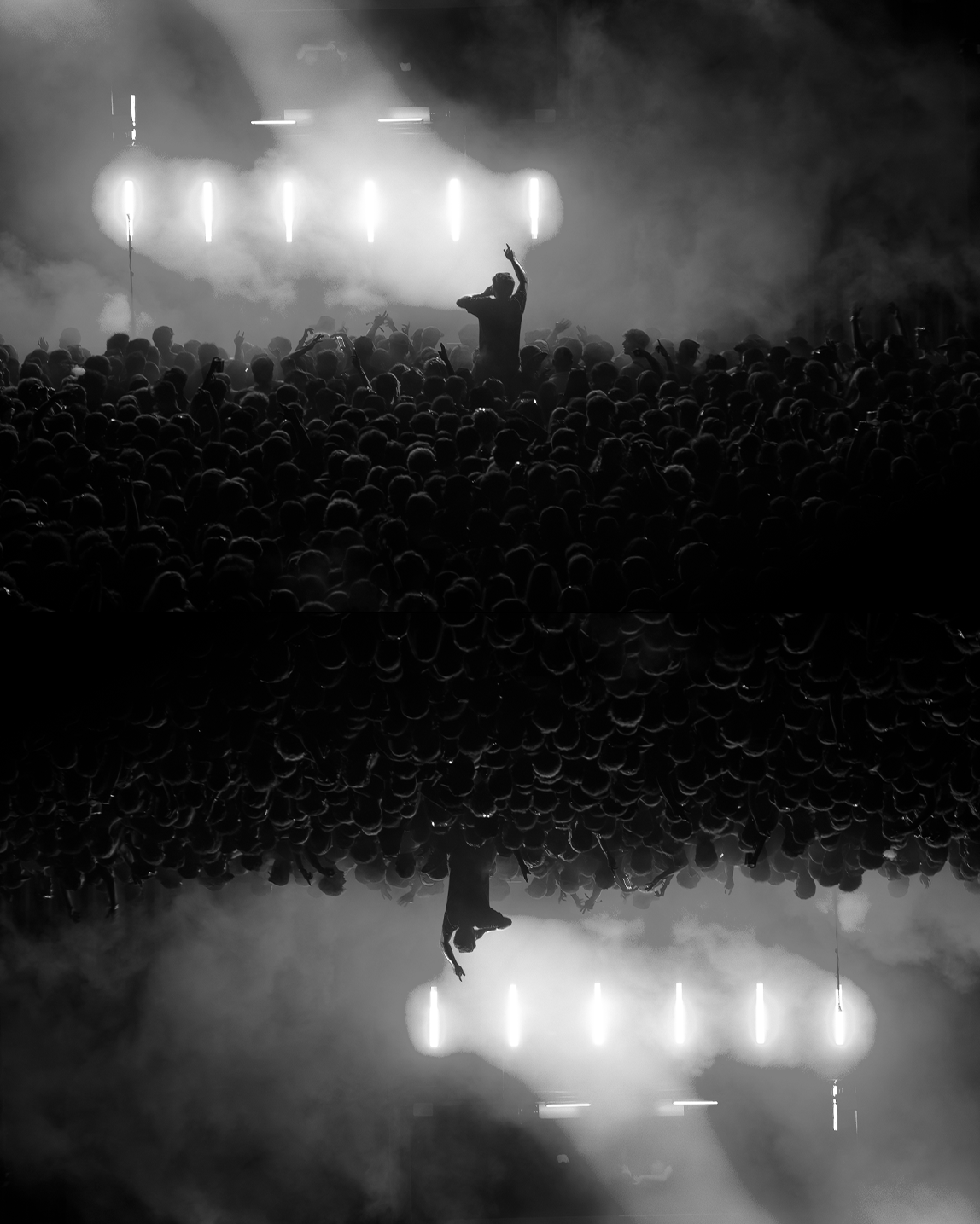 Black and white concert photo with performer raising hand above massive crowd with stage lights.