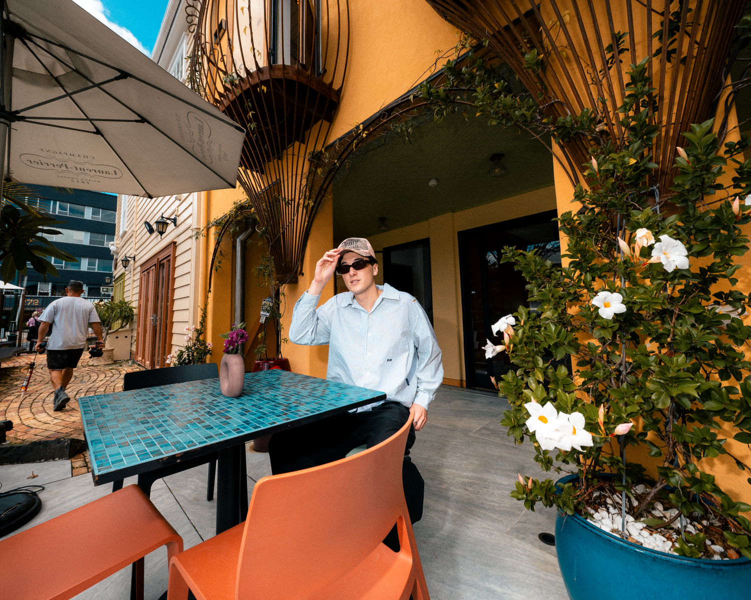 Stylish person wearing cap and sunglasses sitting at turquoise mosaic table at outdoor cafe.