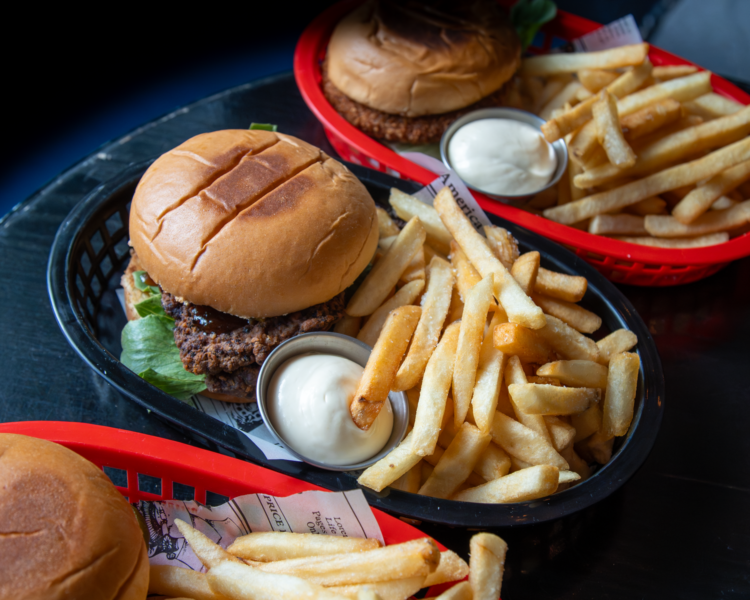 Close-up of a gourmet burger with lettuce and crispy fries served in a black basket with dipping sauce.