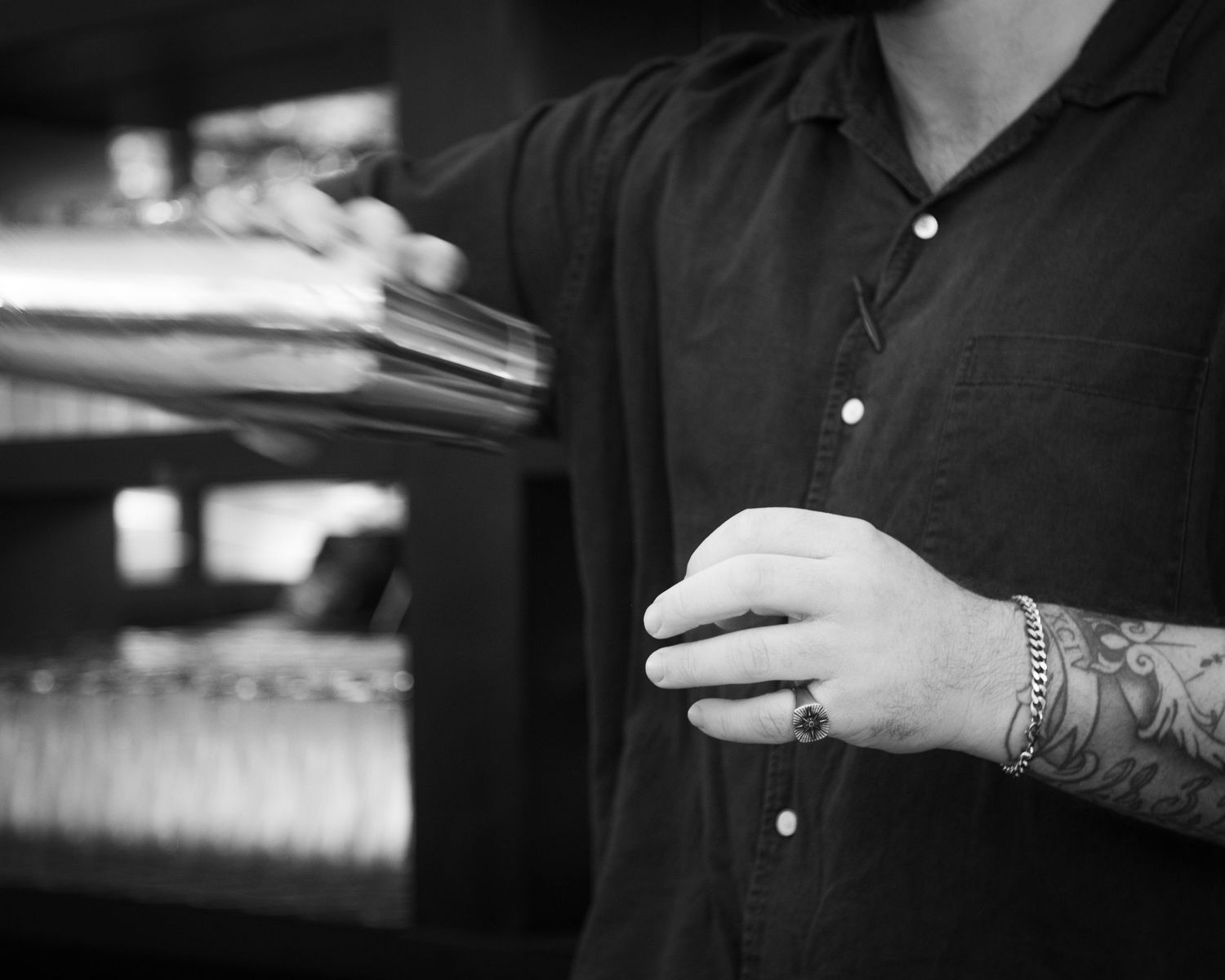 Close-up black and white photo of a tattooed bartender handling drinks at a bar.