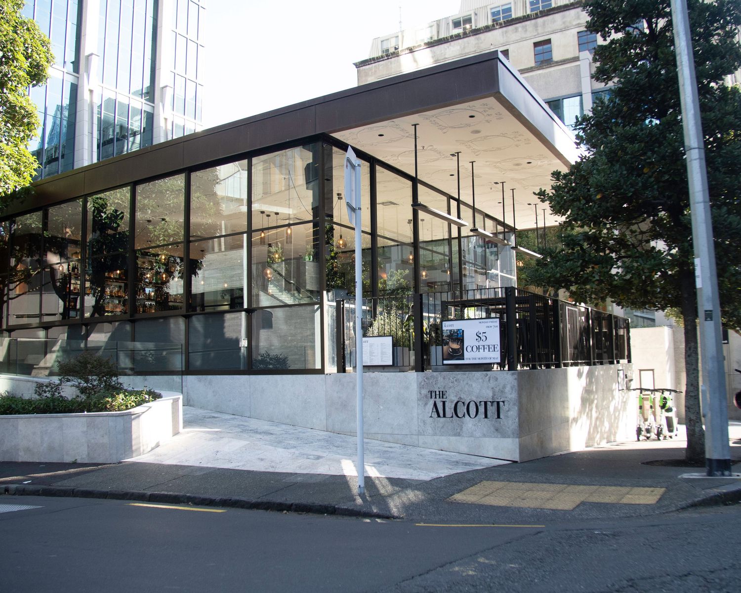Exterior of The Alcott restaurant with floor-to-ceiling glass windows in an urban setting.