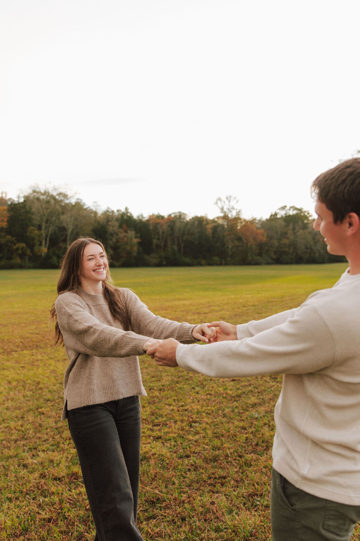 Couple in cozy sweaters dancing and laughing in an autumn field.