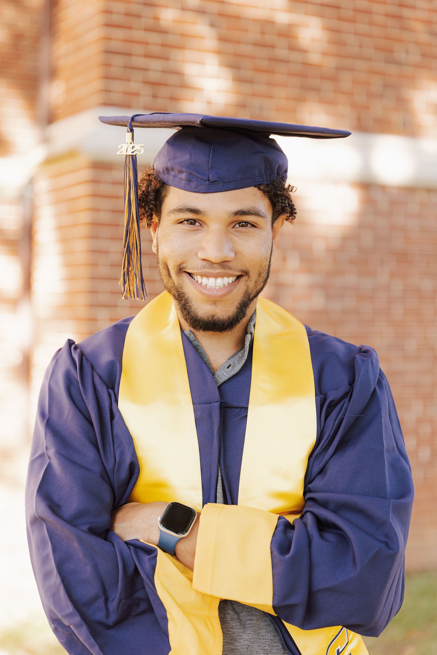 Graduate in navy cap and gown with gold stole smiles in close-up outdoor portrait series.