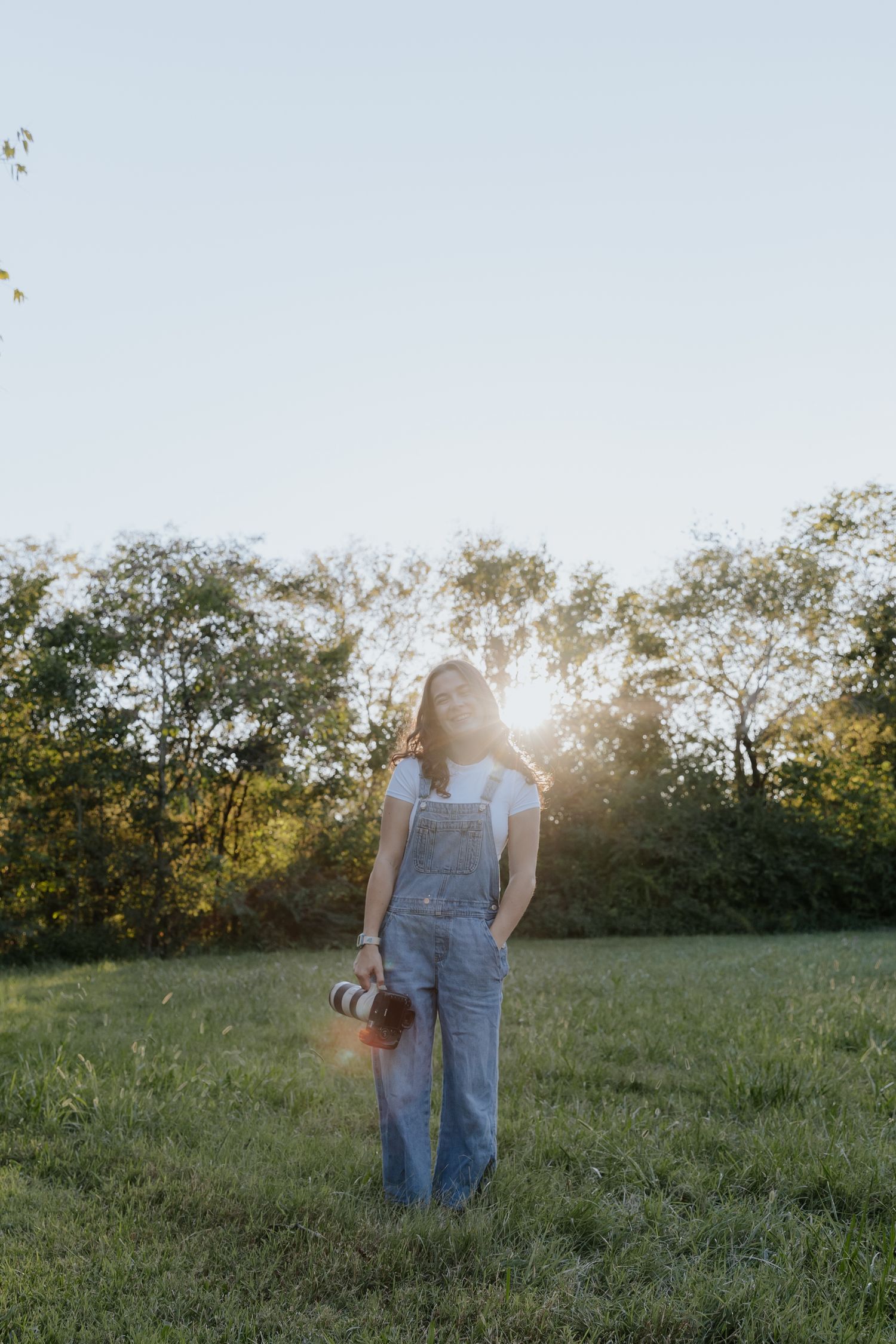 A photographer stands in a sunlit field holding a camera during golden hour.