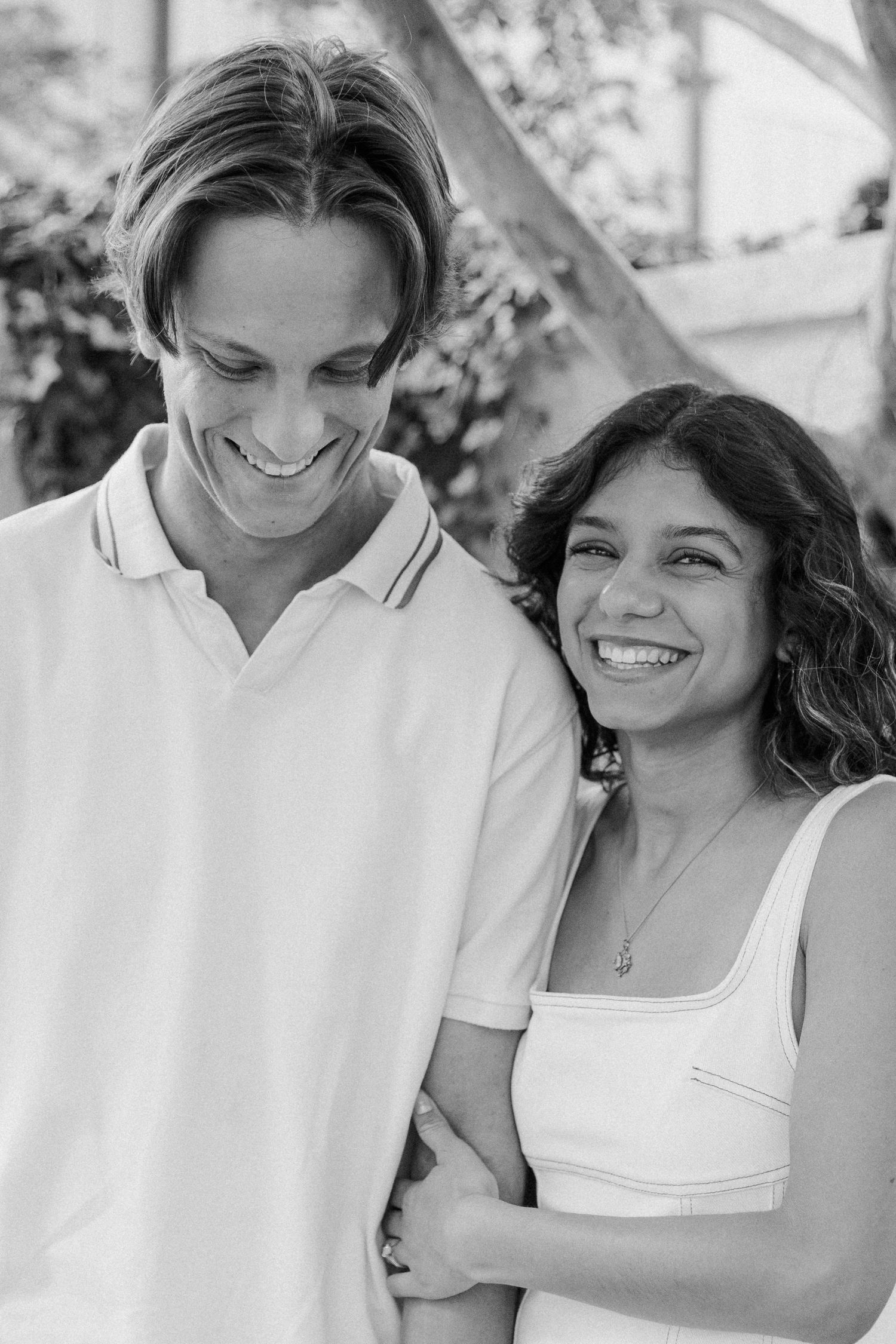 Black and white photo of a smiling couple embracing outdoors, man in polo shirt and woman in white top.