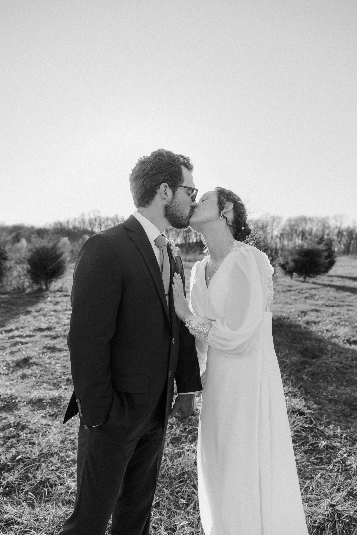Black and white photo of a bride and groom sharing a kiss outdoors on their wedding day.