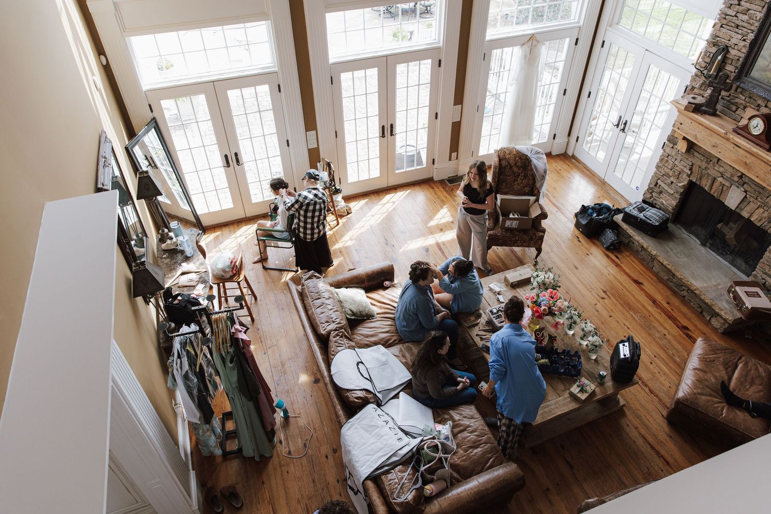 Aerial view of friends and family gathered in a spacious living room with hardwood floors and stone fireplace.