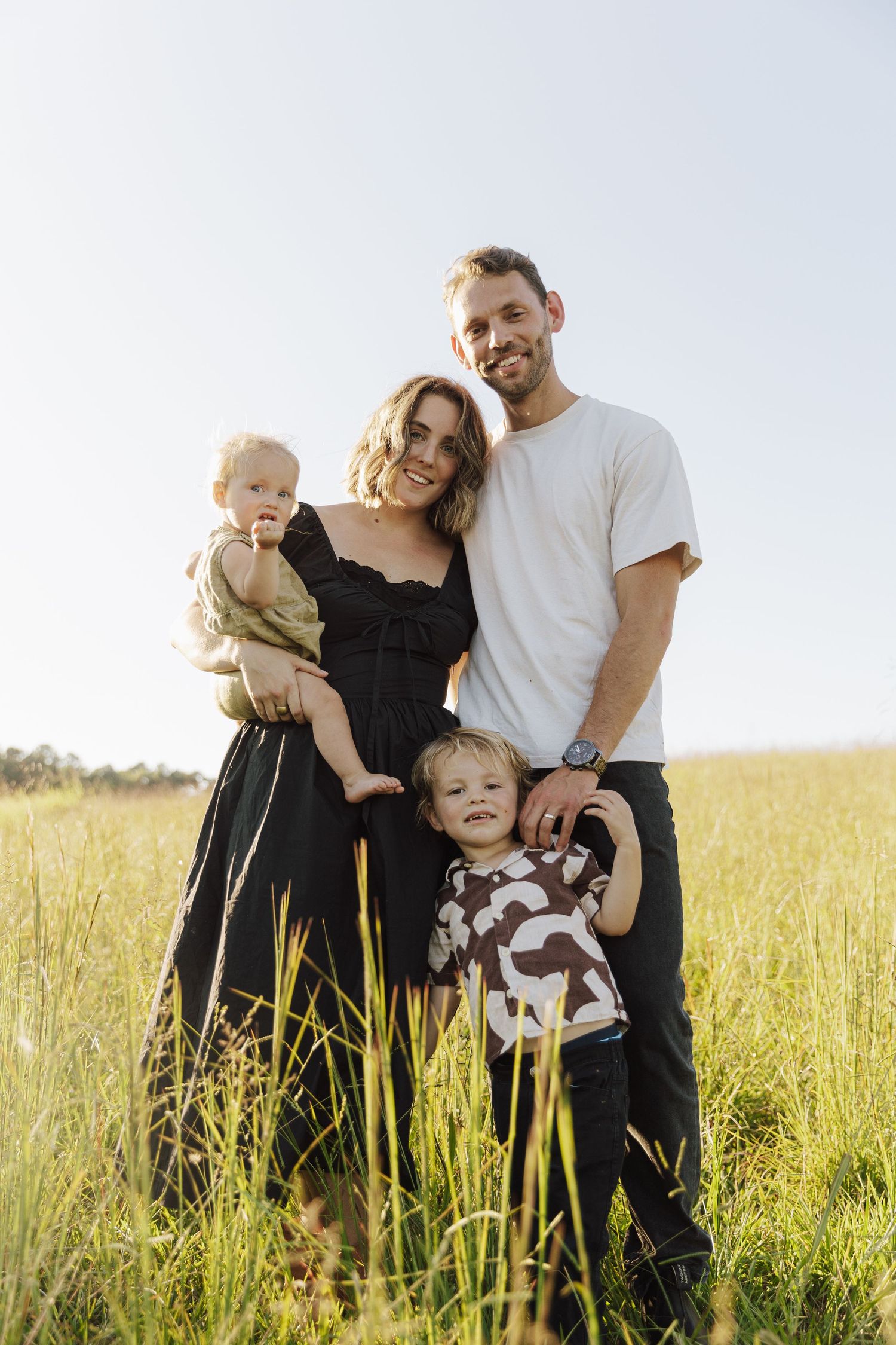 A family stands together in a sun-lit field of tall grass during golden hour.
