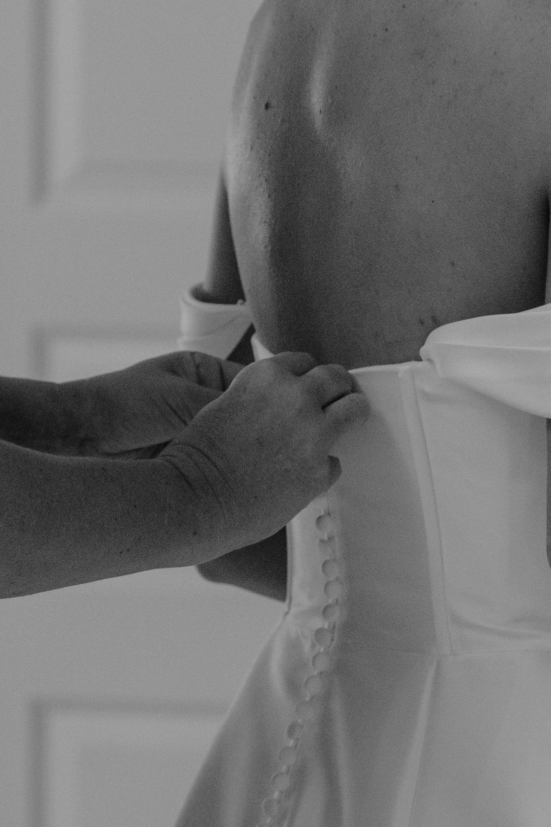 Close-up of buttons being fastened on back of white wedding dress.