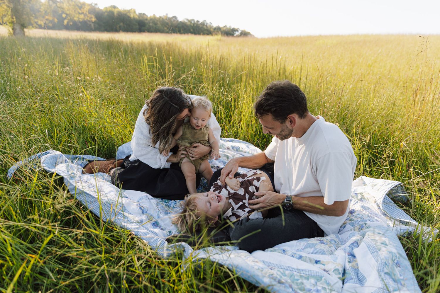 Family laying on a blanket in a golden meadow during sunset while taking photographs.