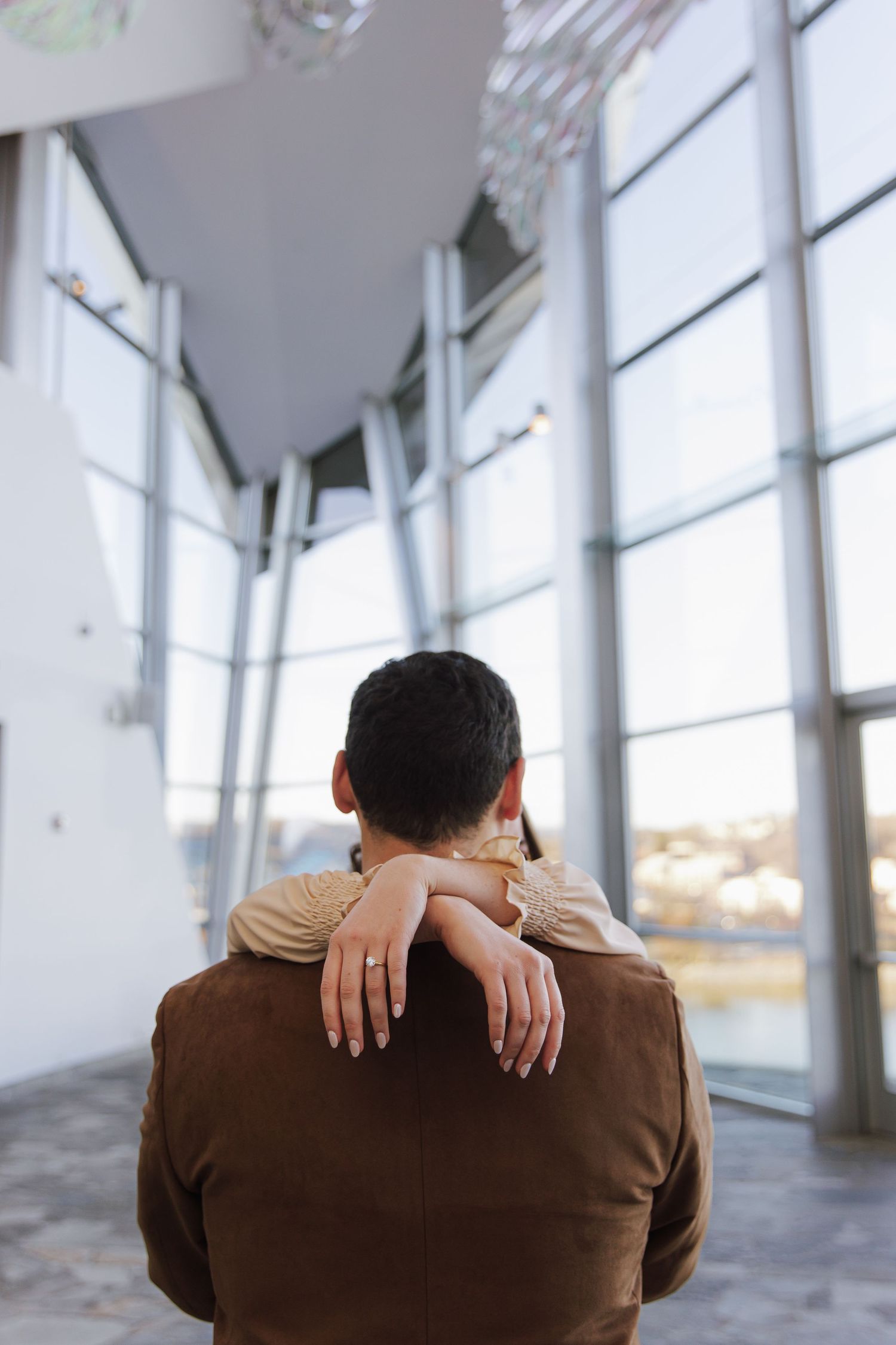 A couple embraces in a modern building with large windows and natural light.