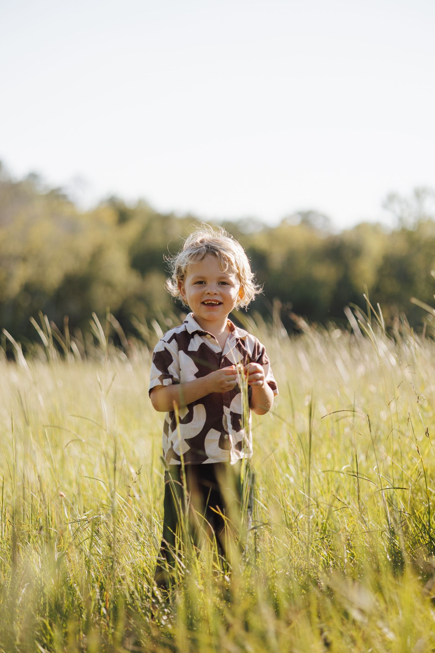A young child plays joyfully in a sunlit meadow with tall golden grass on a warm summer afternoon.