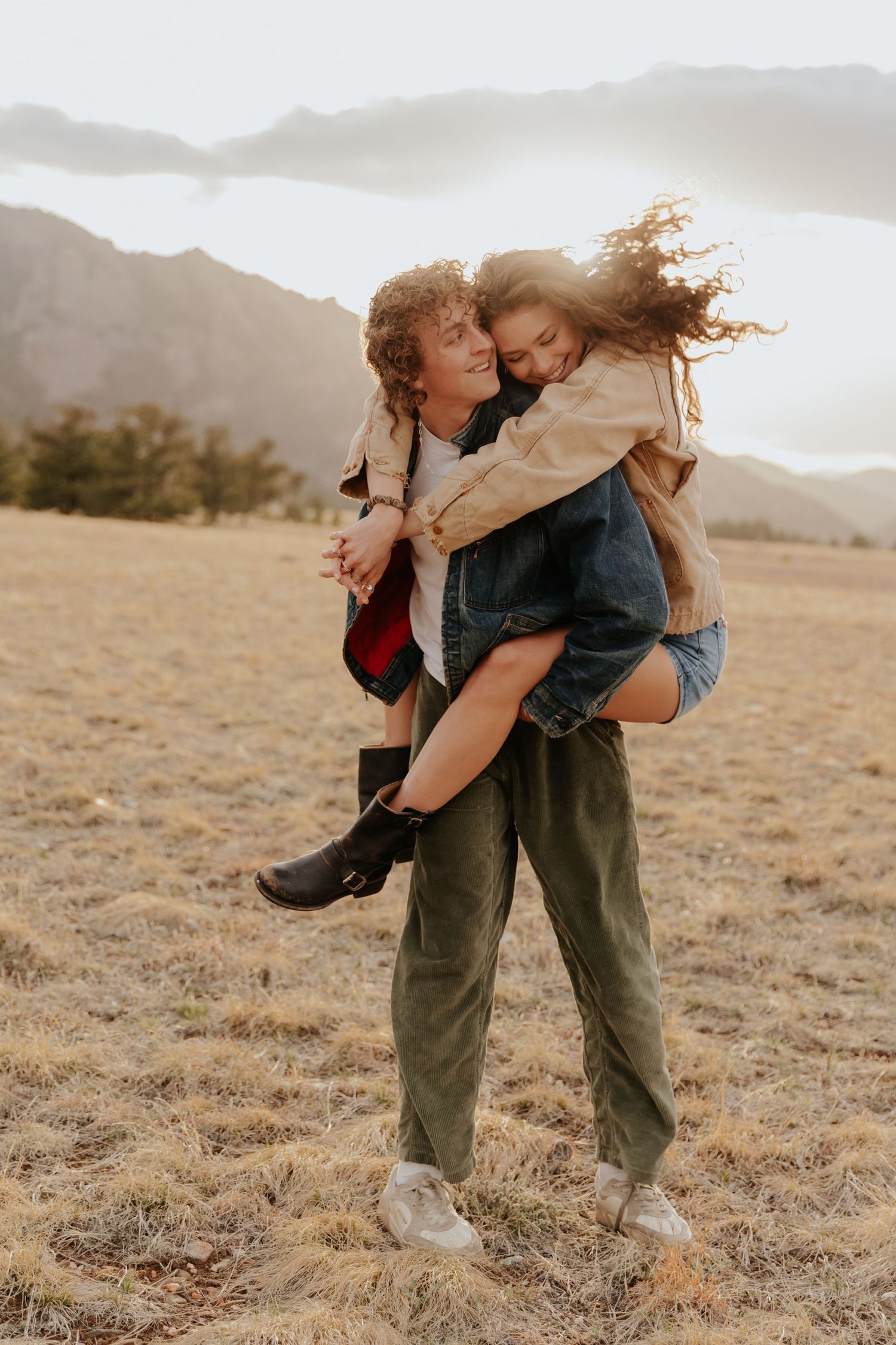 A playful piggyback ride moment captured in a golden field with mountains in the background at sunset.