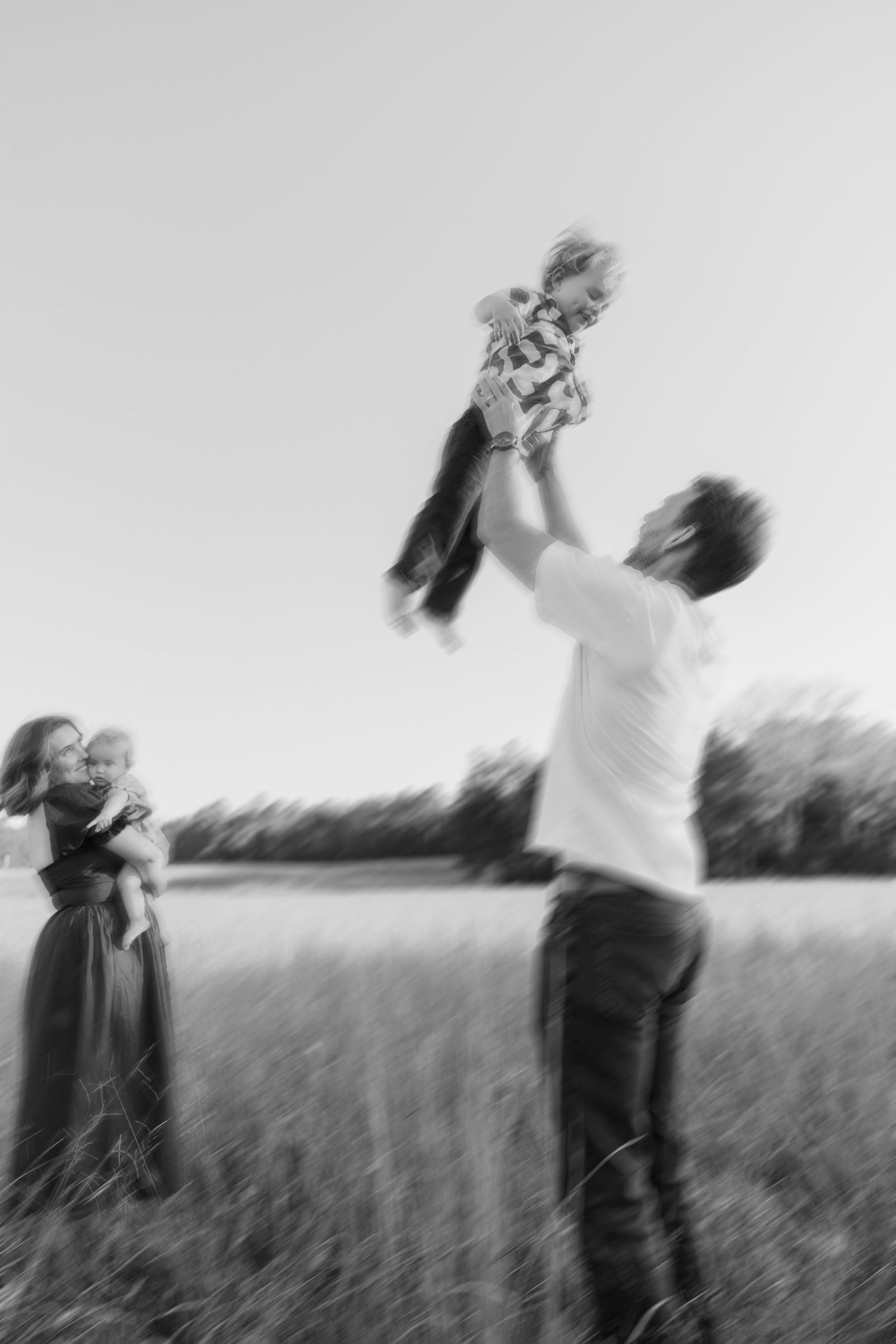 A family photo while the dad is tossing his son in the air and the mom and young daughter and spinning watching them.