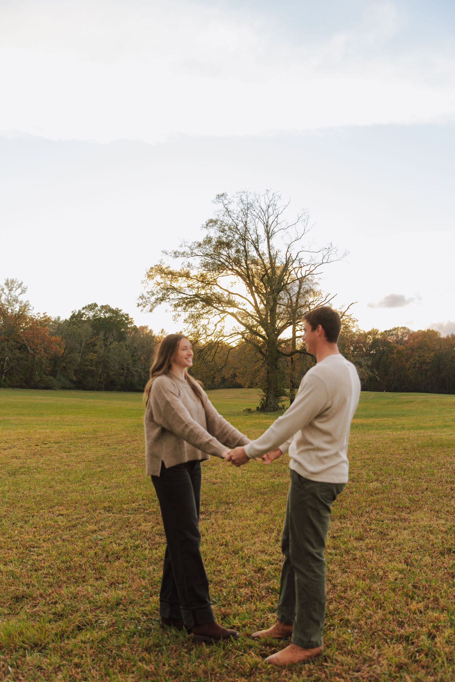 Couple dances and holds hands in a grassy field during sunset.