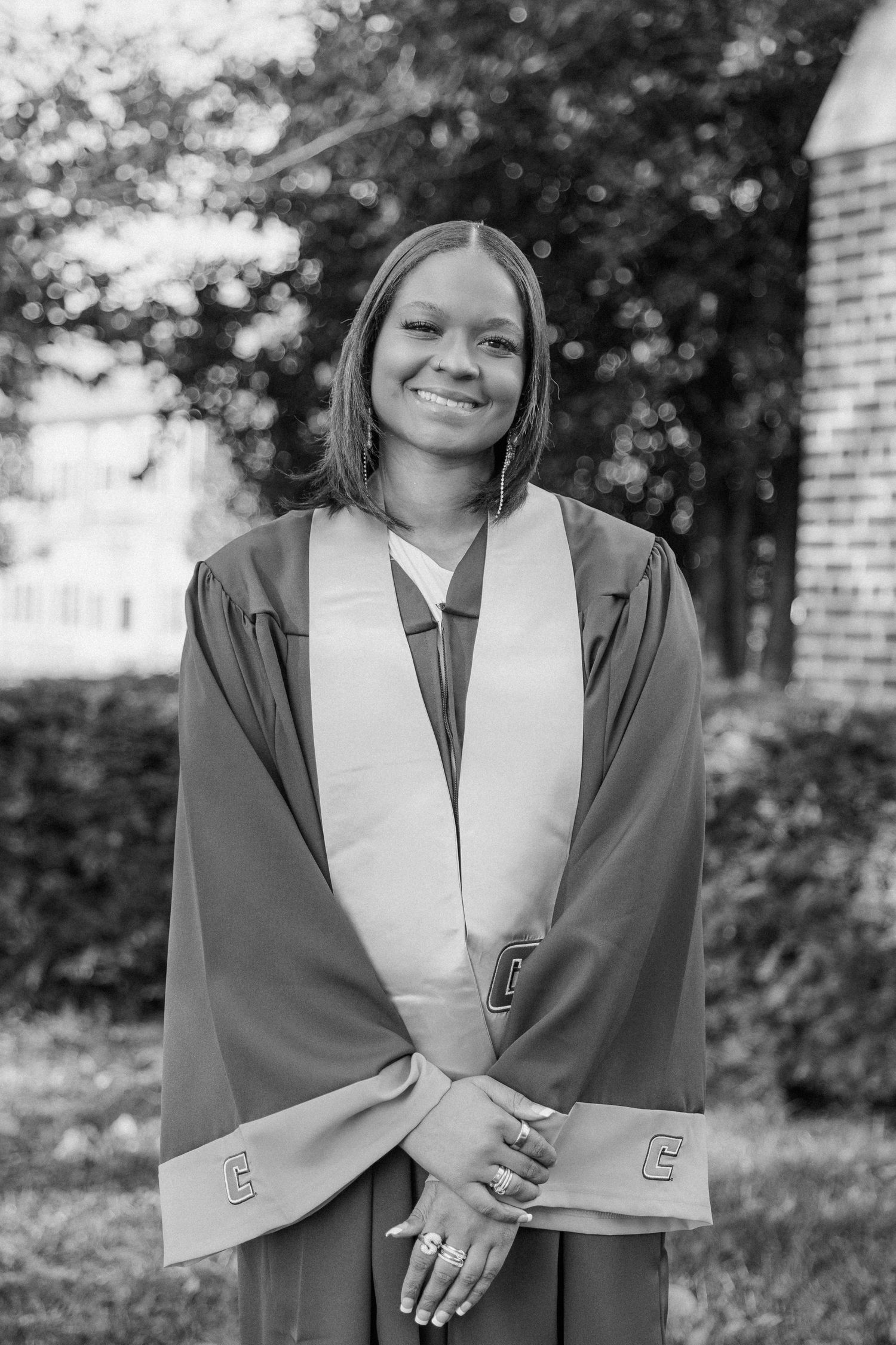 Graduate wearing navy cap and gown with gray shawl poses in black and white outdoor portrait series.