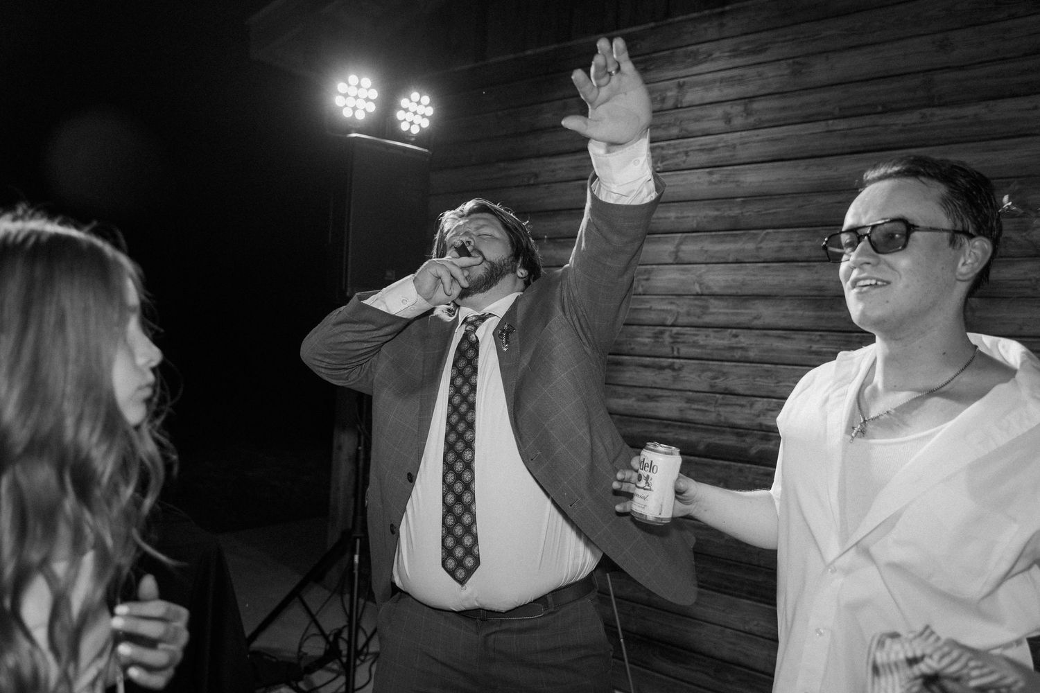 Black and white photo of men celebrating at a wedding reception, one raising hand and drinking.