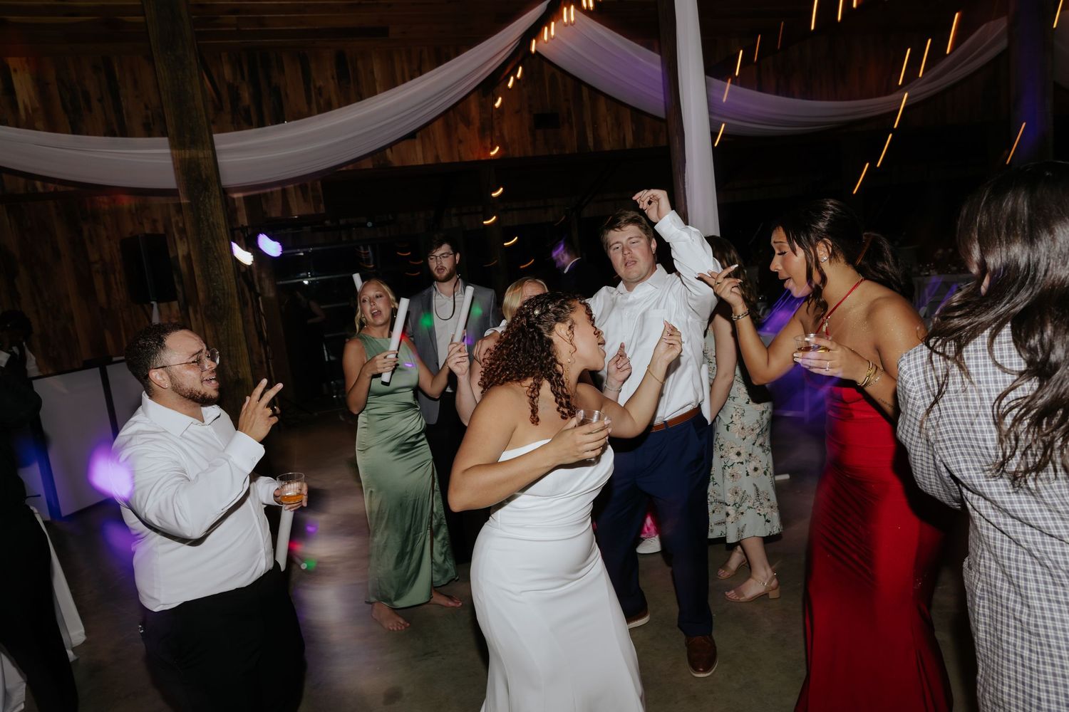 Wedding guests dancing at reception in dimly lit rustic barn venue.