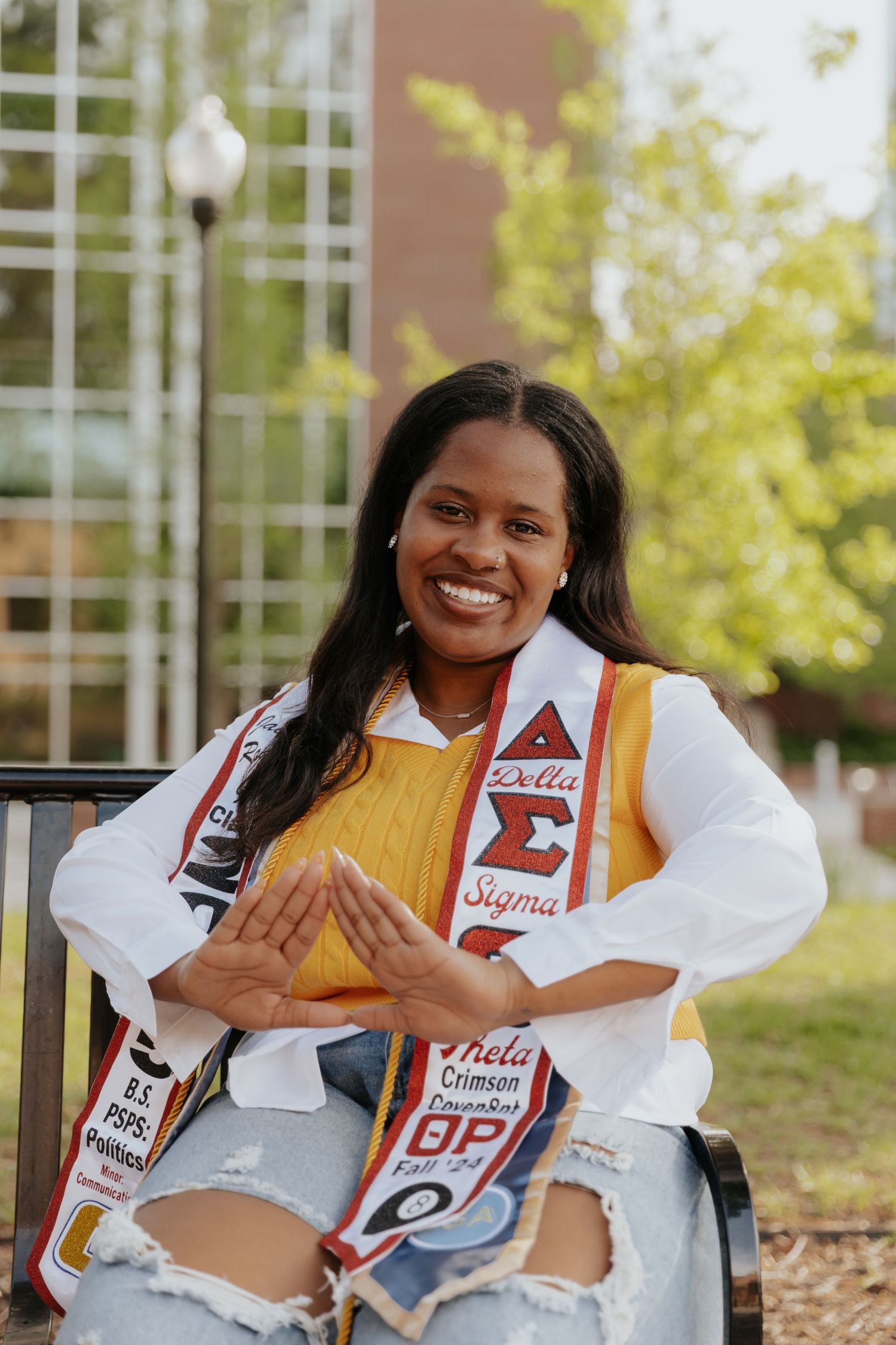 Cheerleader in white and red uniform poses outdoors on campus while sitting on steps.