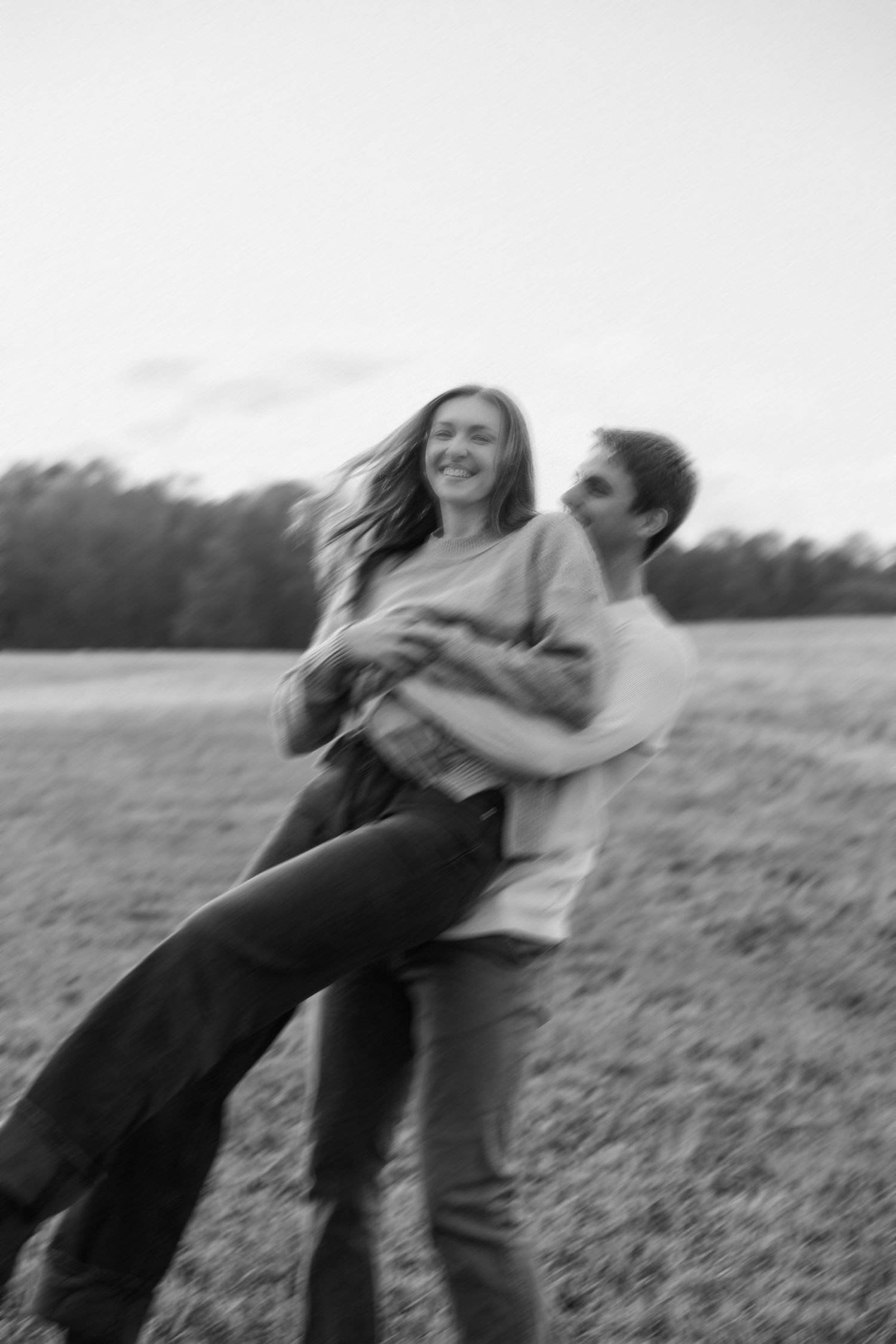 Playful couple spins and dances together in a blurred motion sequence in an open field.