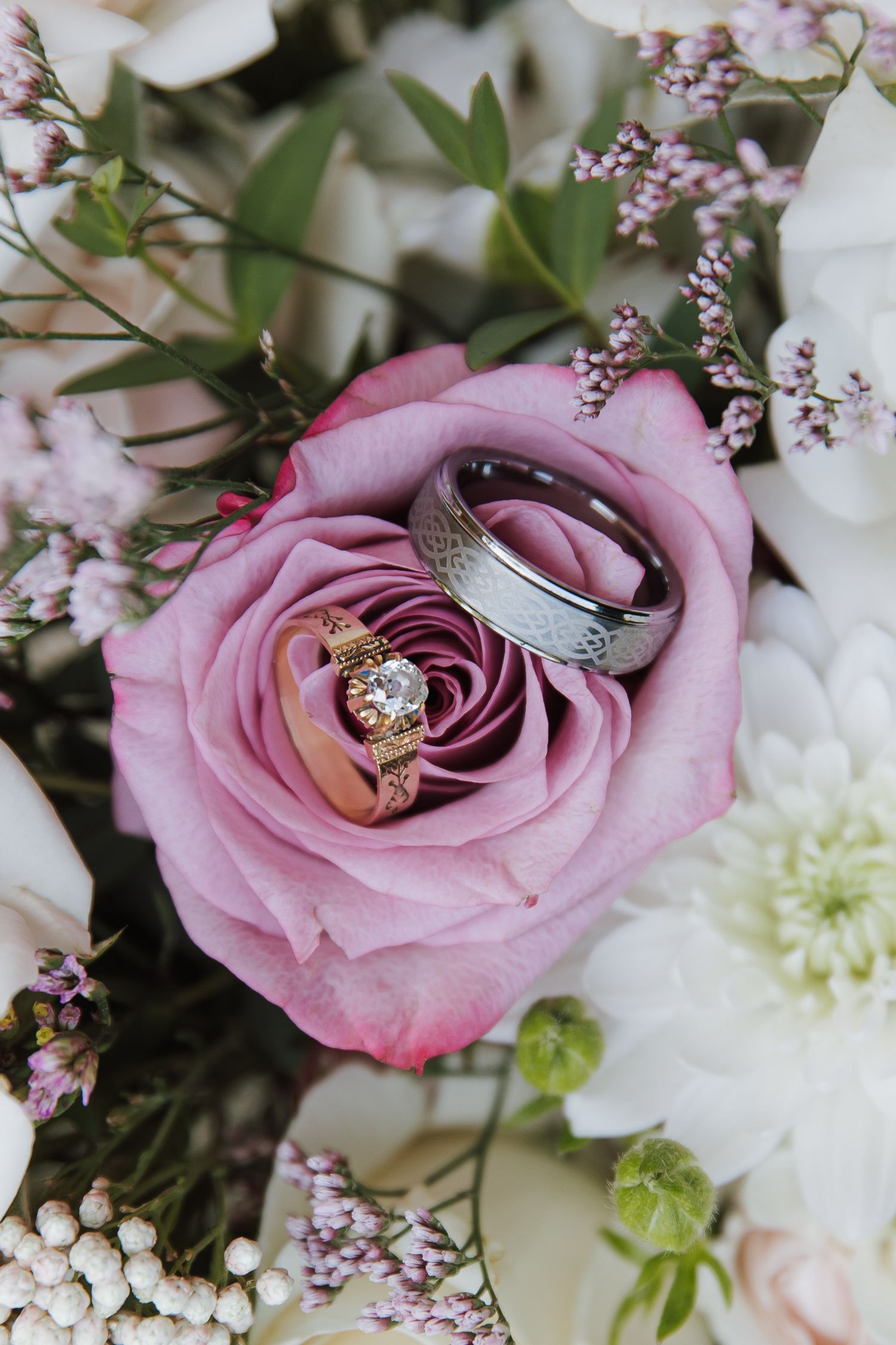 Wedding rings nestled in a pink rose bouquet with white flowers and greenery, symbolizing love and commitment.