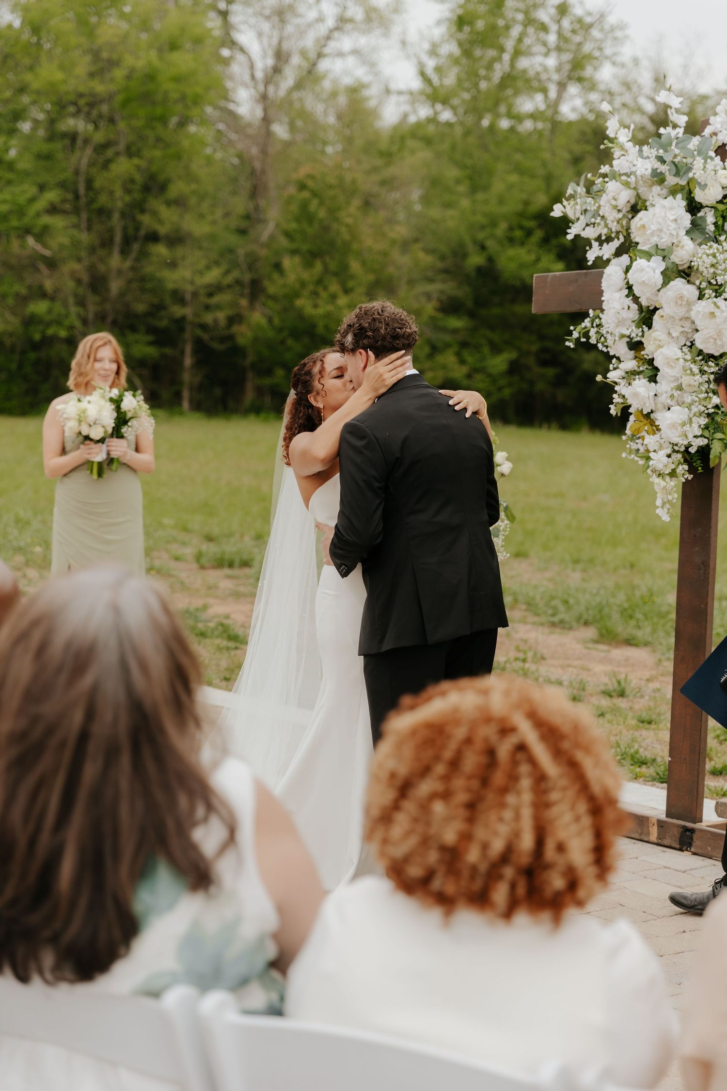 Wedding guests watch ceremony from rows of white chairs at outdoor venue.