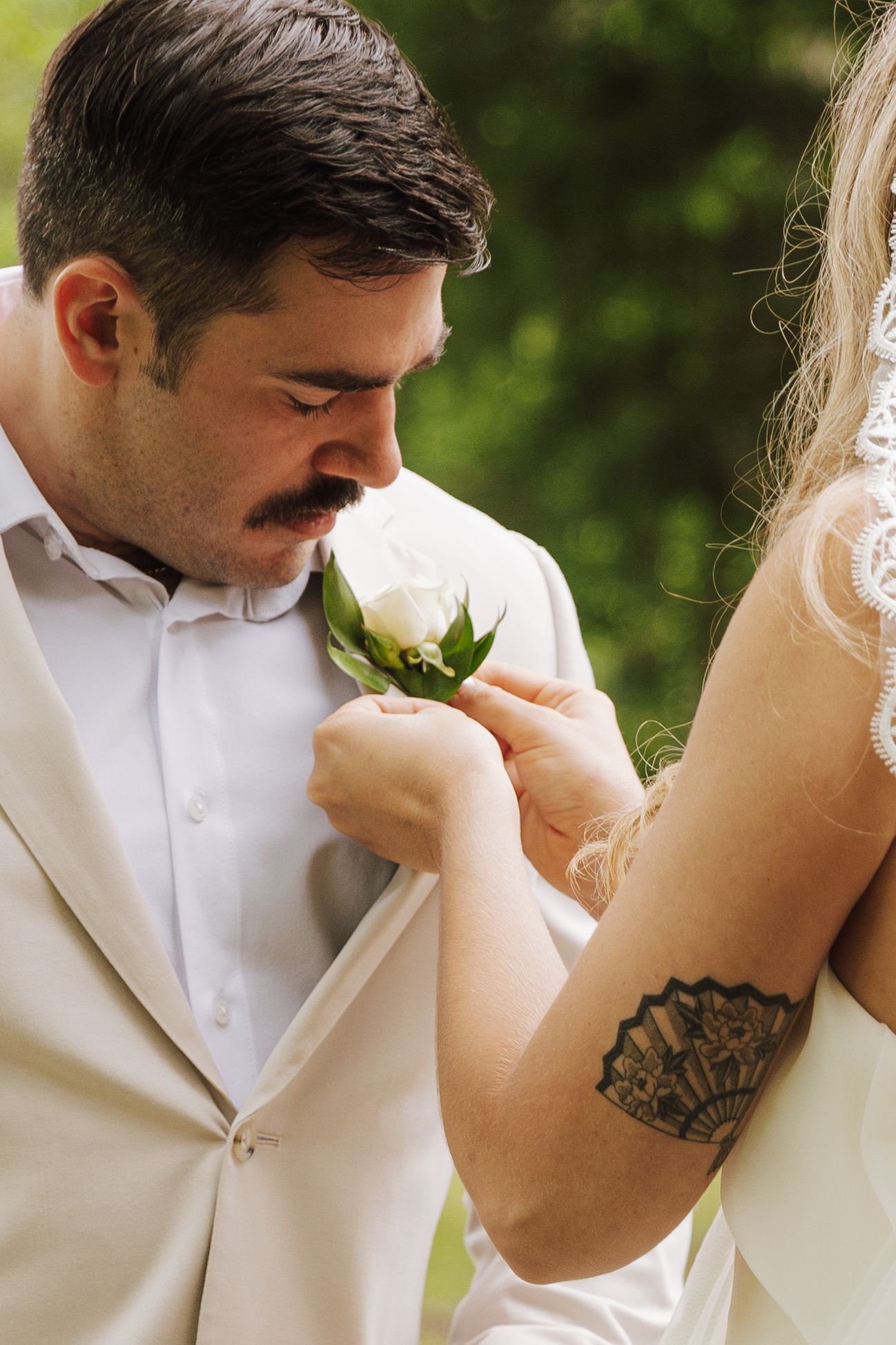 Close-up detail shot of a white boutonniere rose being pinned on a cream colored suit jacket.