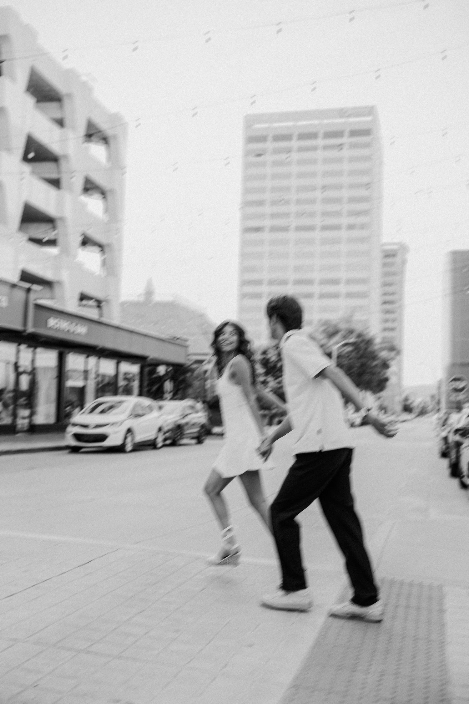 Black and white photo of a couple holding hands and walking together on a city street with tall buildings.