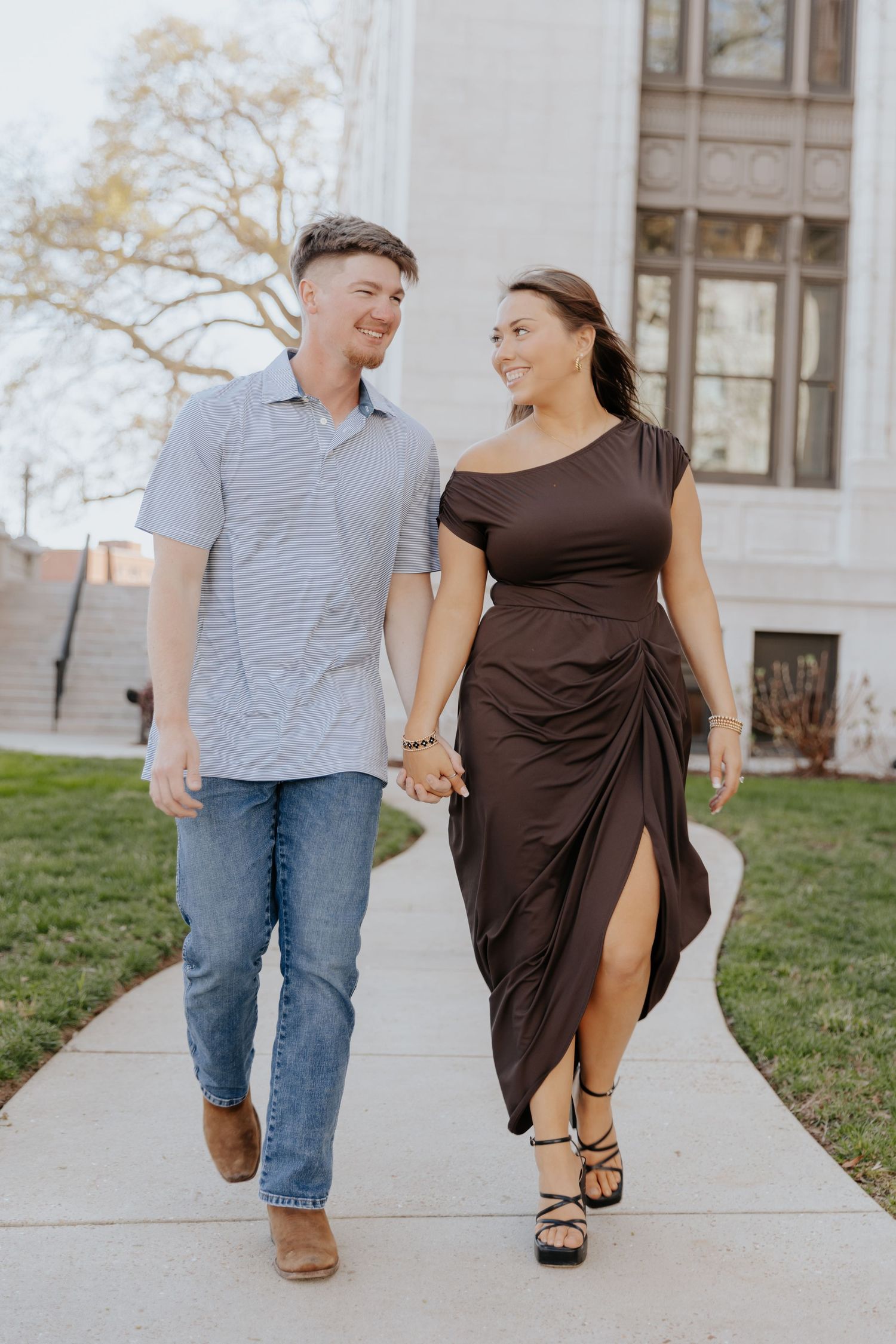 A couple walks hand in hand along a concrete path while wearing casual attire on a sunny day.