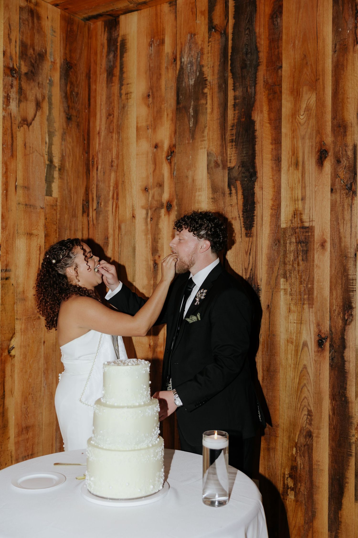Wedding couple cuts cake together in rustic wooden venue.