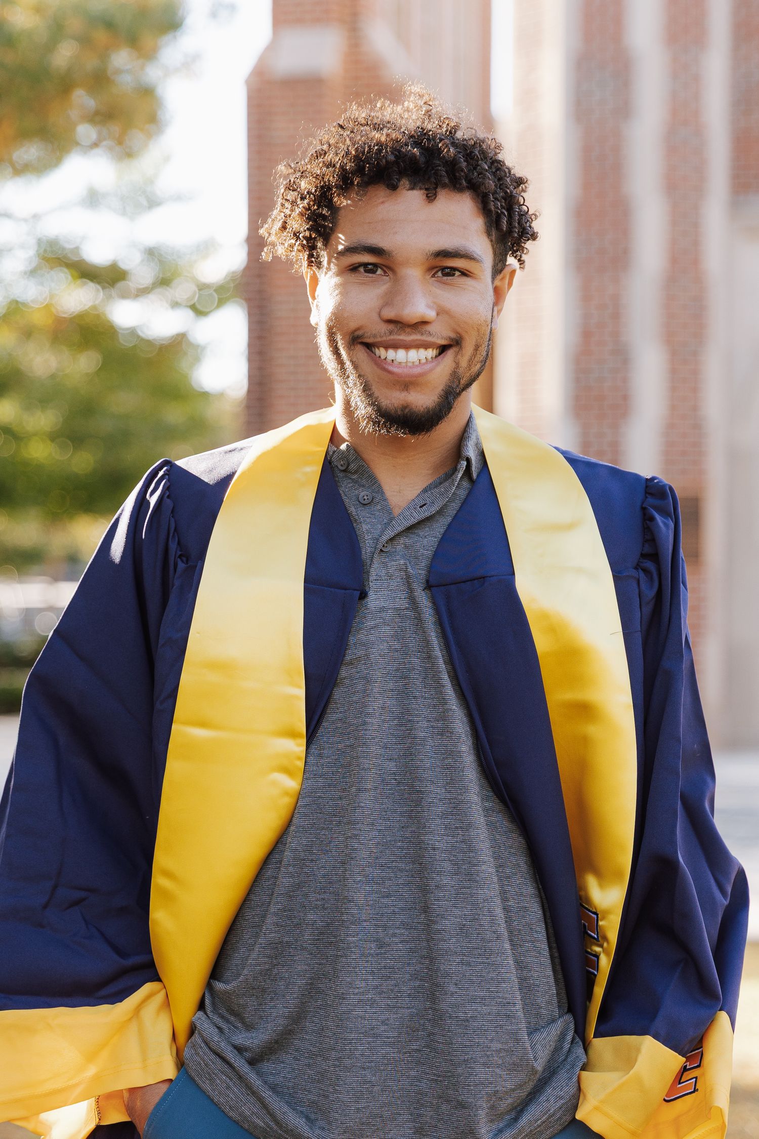 A person in graduation attire wearing a navy blue gown and yellow stole smiles in a series of outdoor portrait shots.