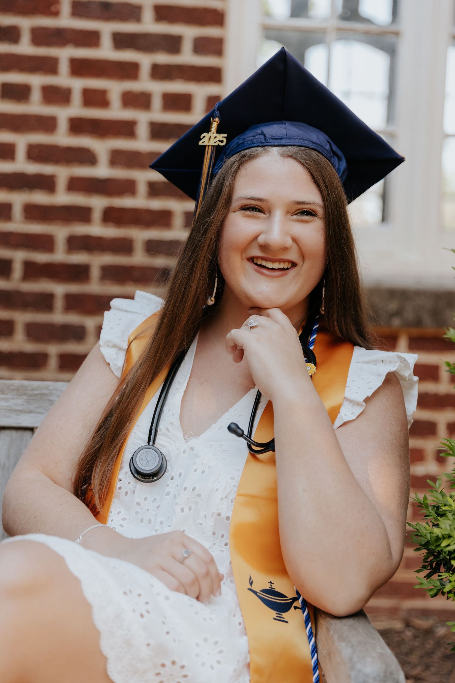 A nursing graduate in white dress and academic regalia poses for graduation photos.