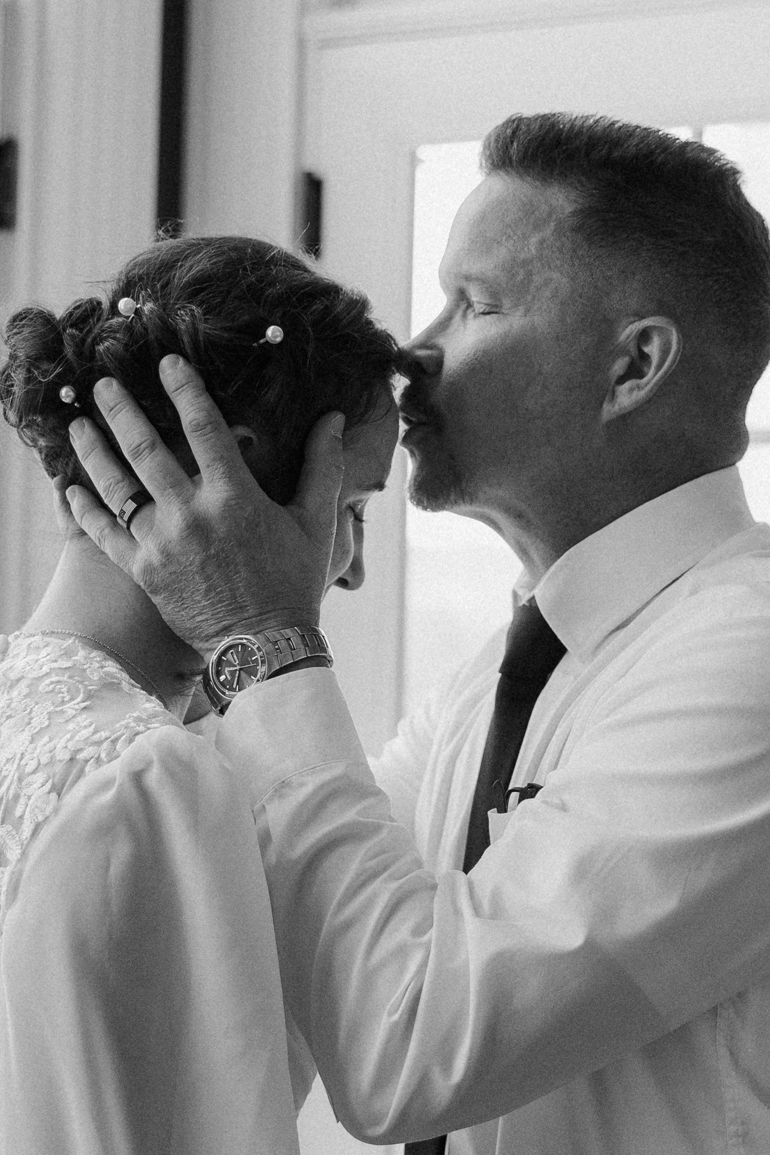 Row of groomsmen in white shirts adjusting their ties in a synchronized black and white photo.